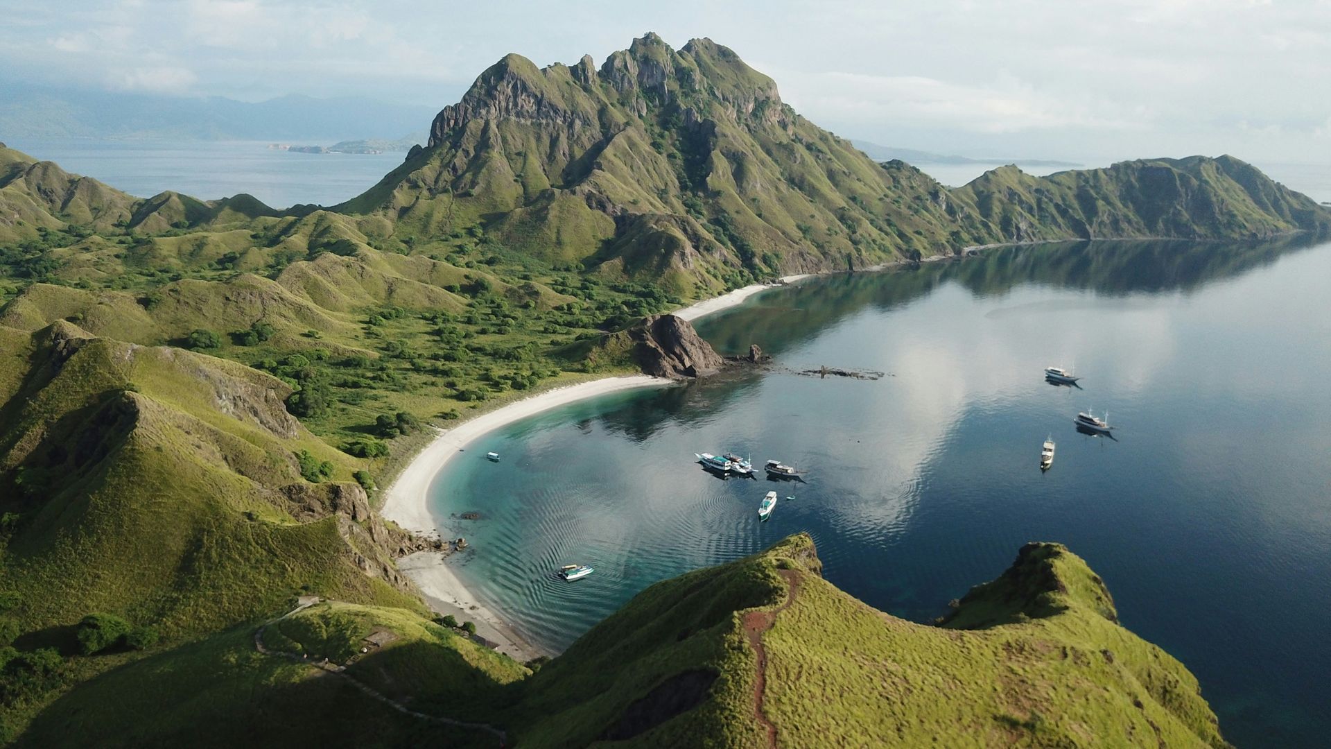 An aerial view of Komodo, Indonesia, with boats in the water and mountains in the background.