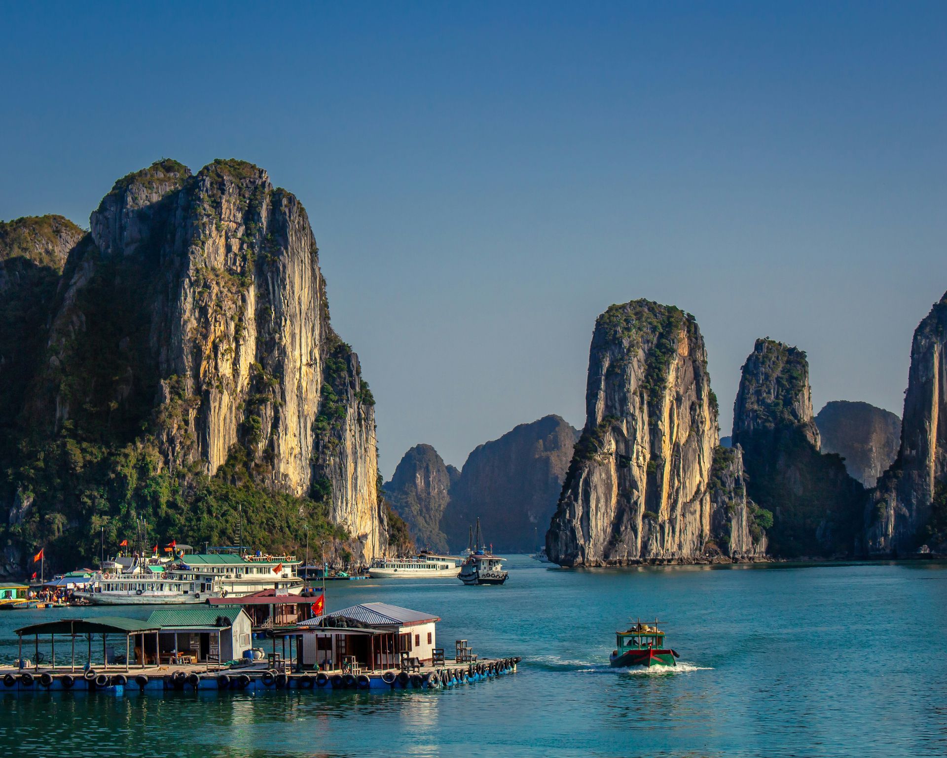Rocky islands rise from blue water, boats and floating houses in Halong Bay, Vietnam.