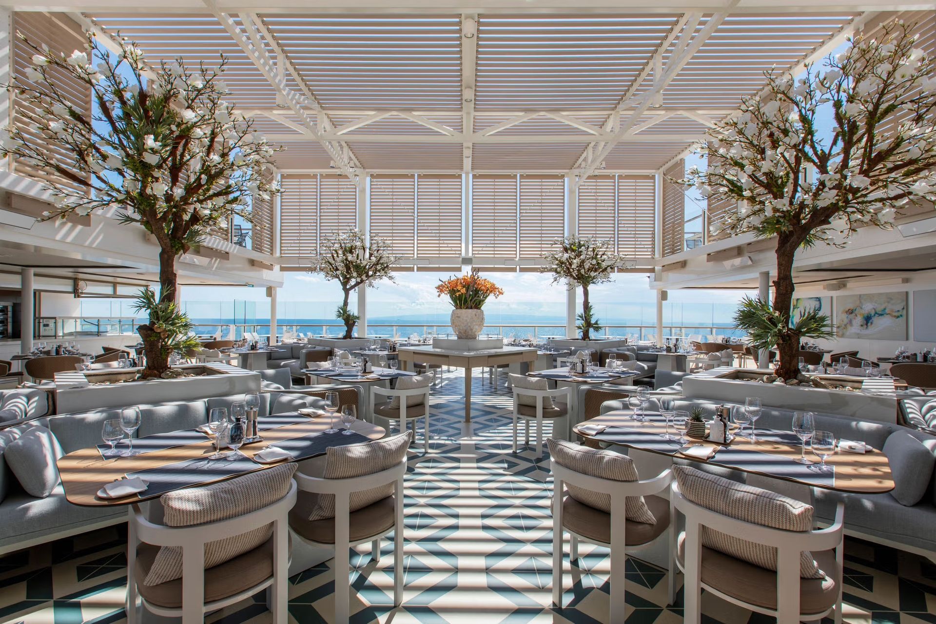 A large dining room with tables and chairs and a view of the ocean on Silversea's Silver Ray cruise ship.
