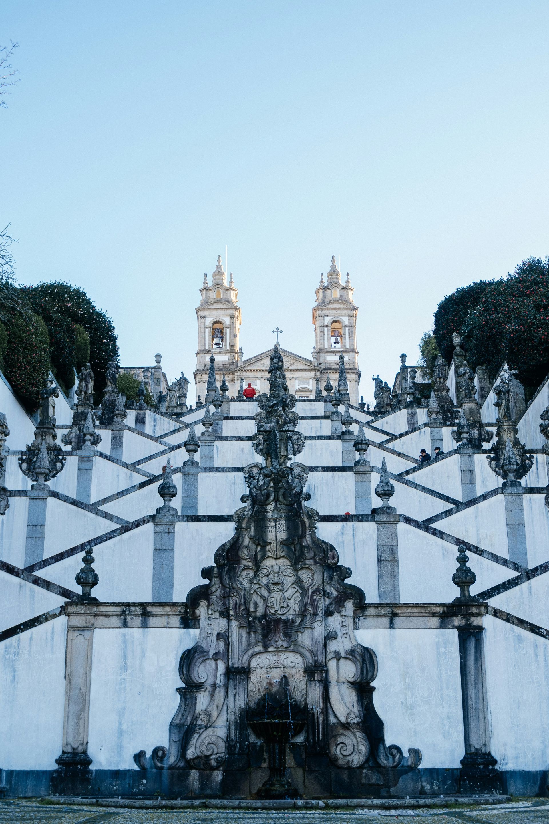 A long, ornate white staircase leads up to a church with twin towers, against a blue sky in Braga, Portugal.