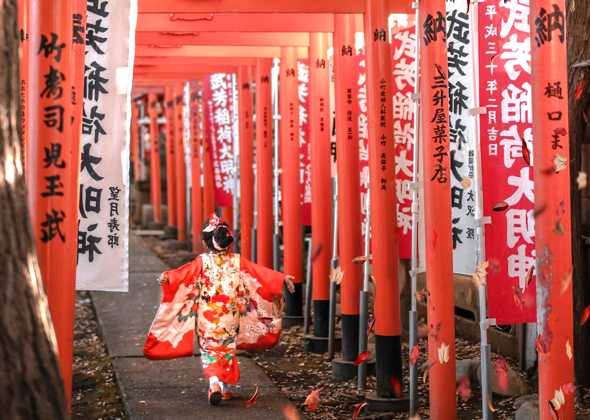 A person in a colorful kimono walks through a tunnel of red torii gates lined with banners in Japan.