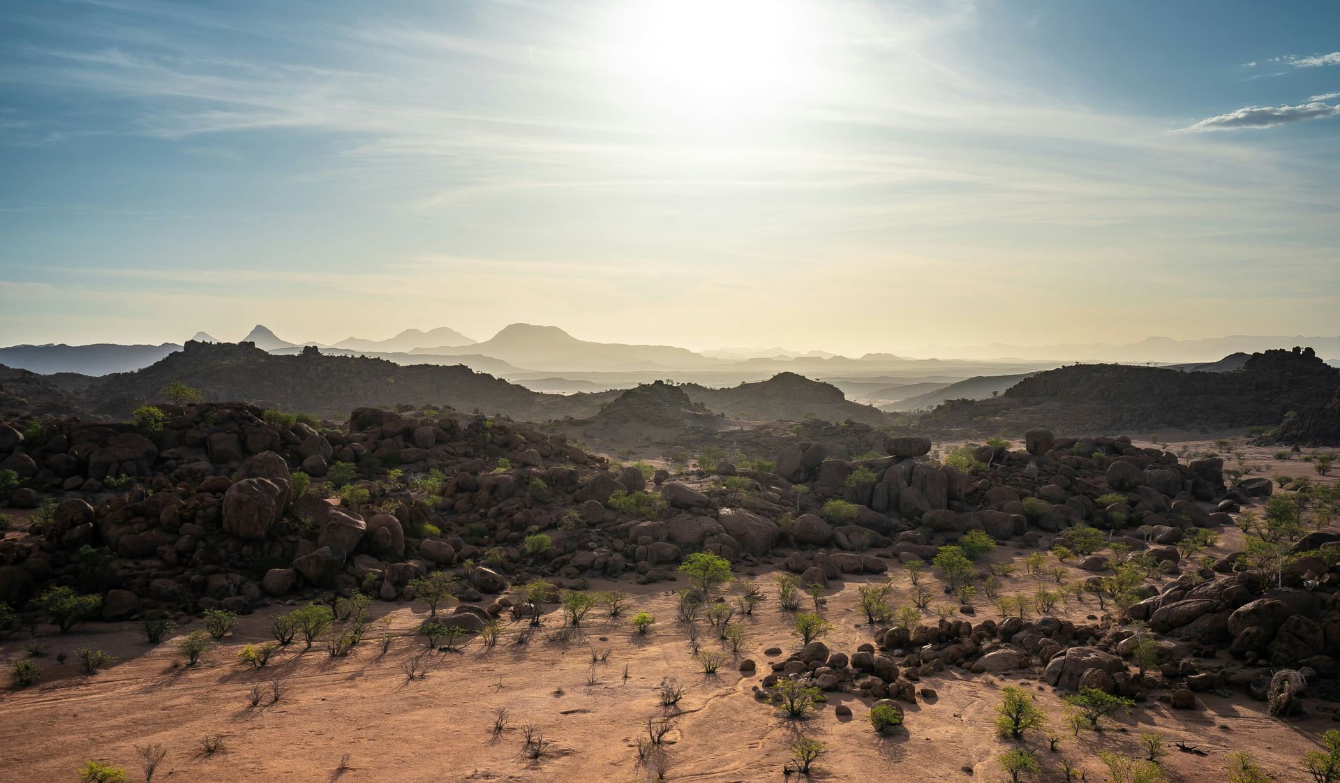 Sunlit landscape of rocky hills and sparse vegetation in Damaraland, Namibia.