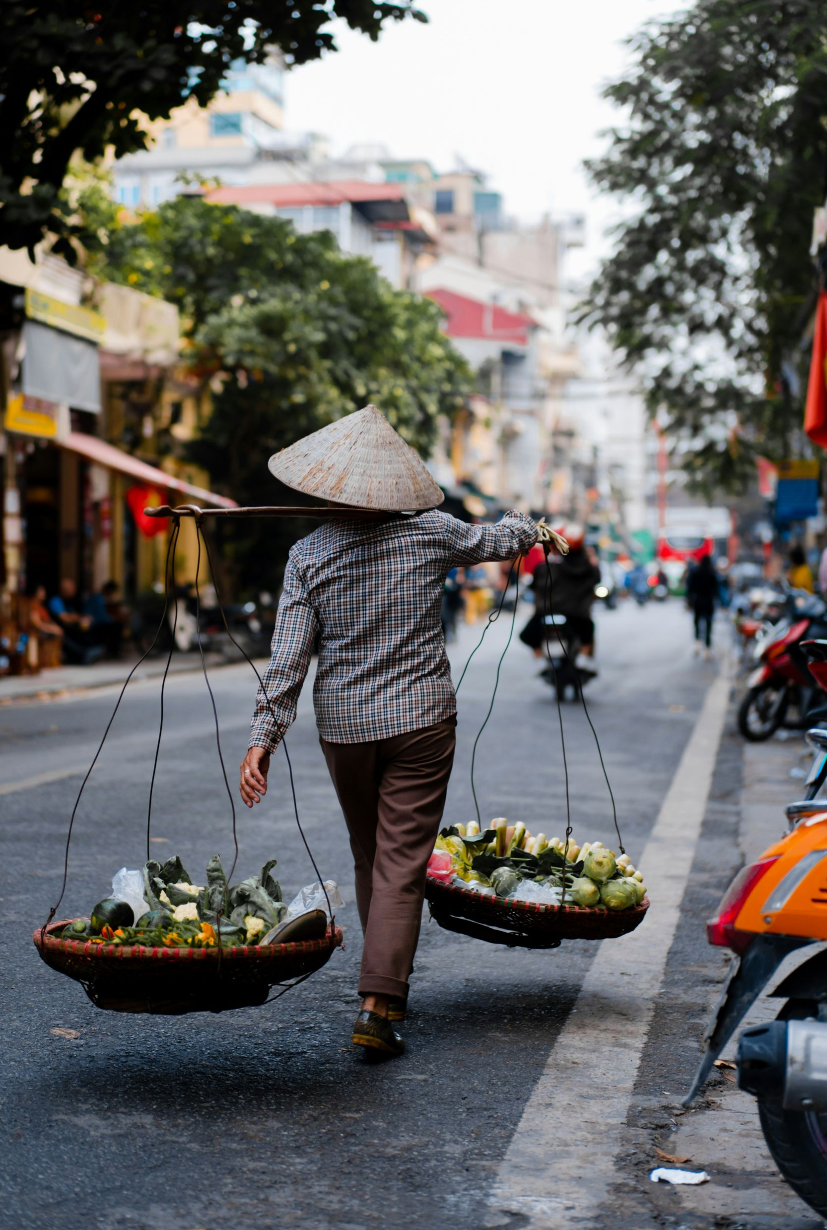 Woman in traditional hat carrying baskets of fruit on a street in Vietnam.