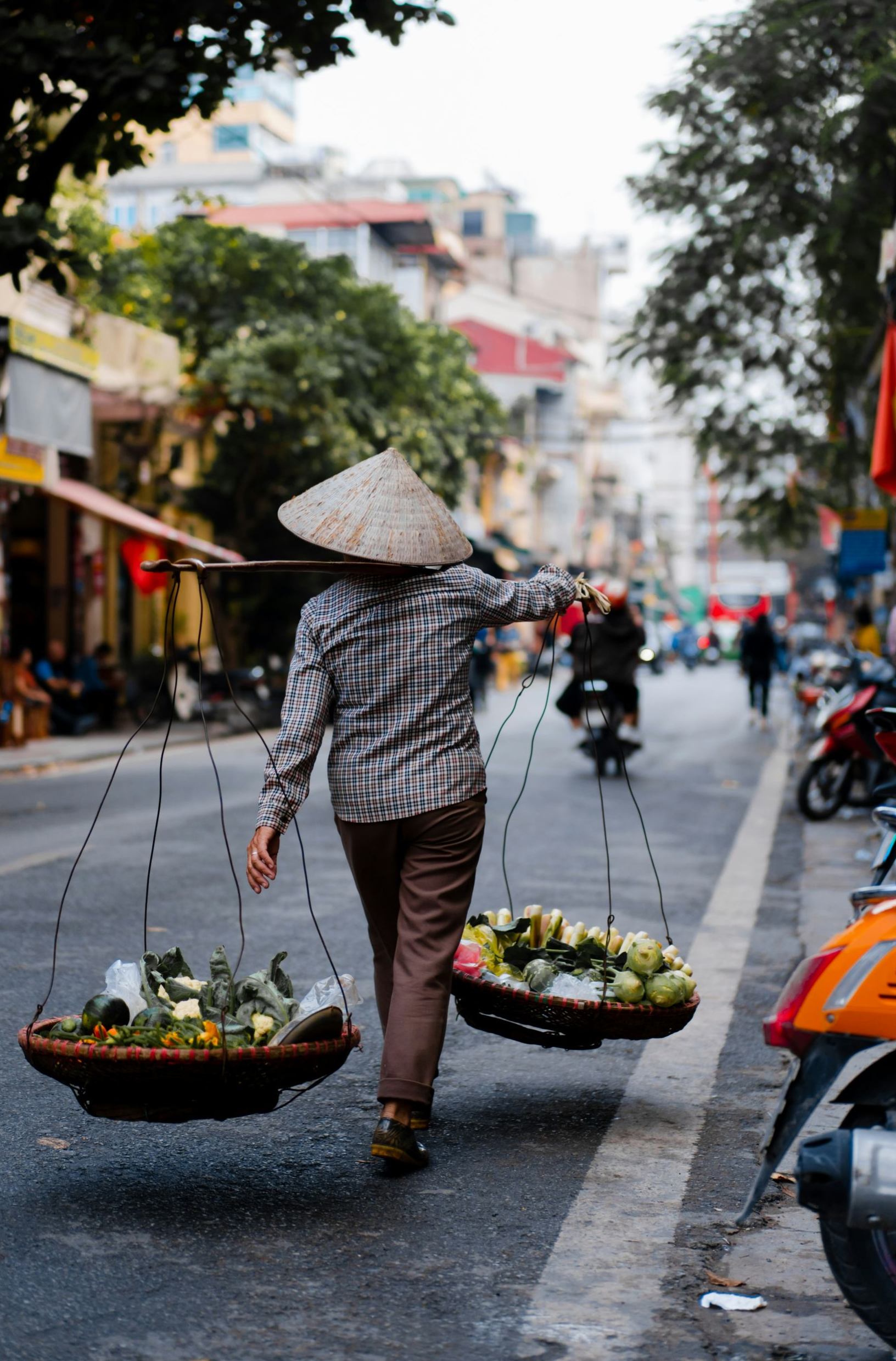 Woman in traditional hat carrying baskets of fruit on a street in Vietnam.