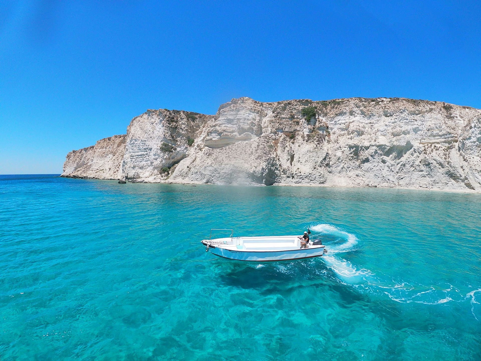 A boat is floating on top of a clear blue ocean in Crete, Greece.