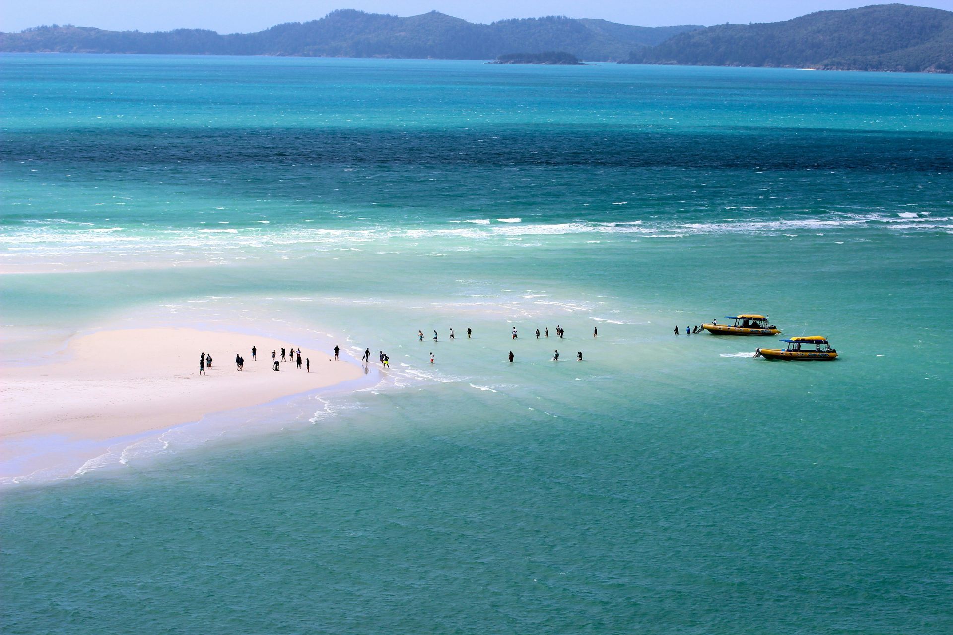 A group of people are standing on a sandy beach in the middle of the ocean in the Whitsundays, Australia. 