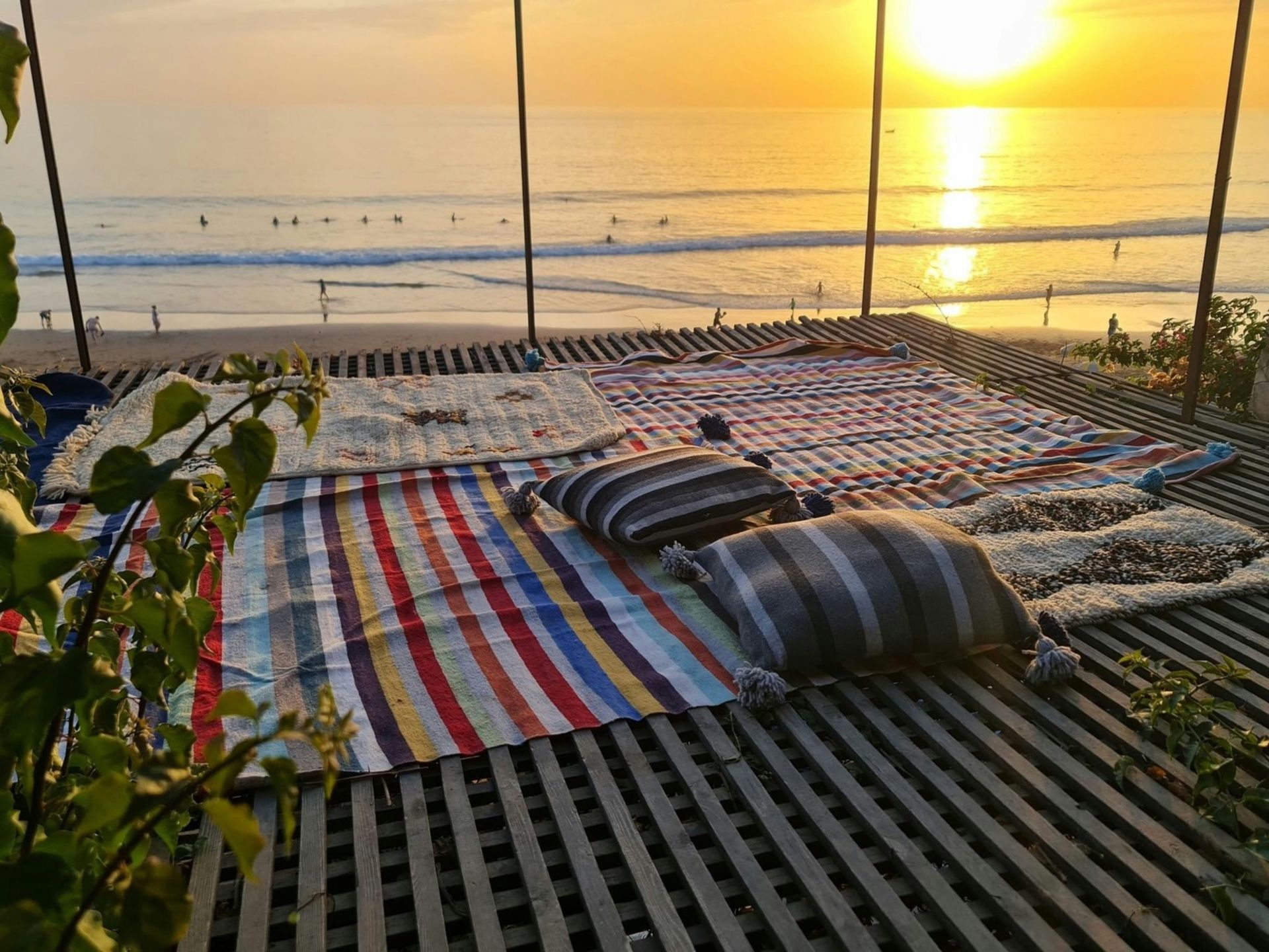 A wooden deck with a blanket and pillows on it overlooking the ocean at sunset in Taghazout, Morocco.