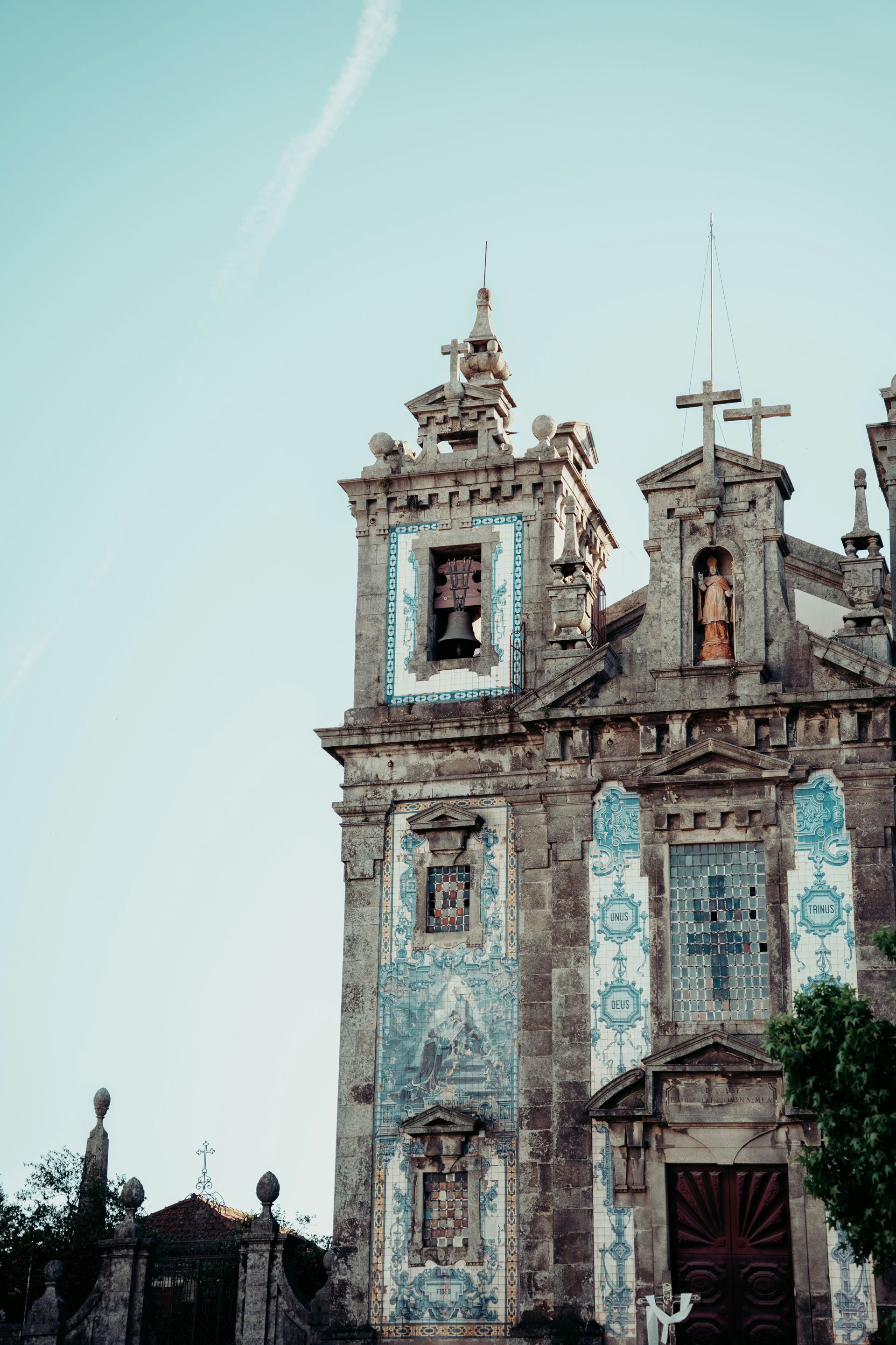 Ornate stone church with blue azulejos tile accents under a pale blue sky in Porto, Portugal.