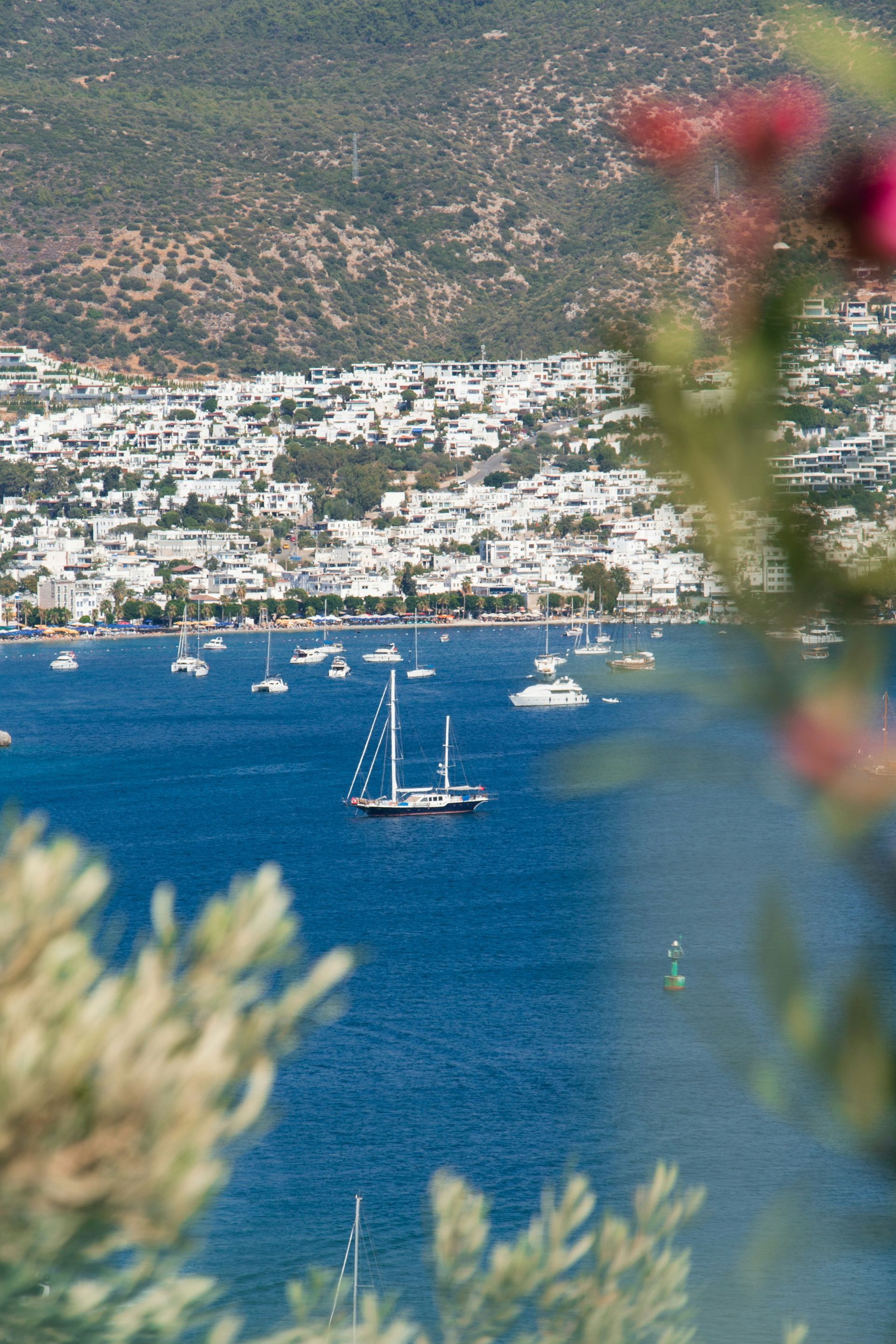Sailboat on blue water with town and mountains in background in Bodrum, Turkey.