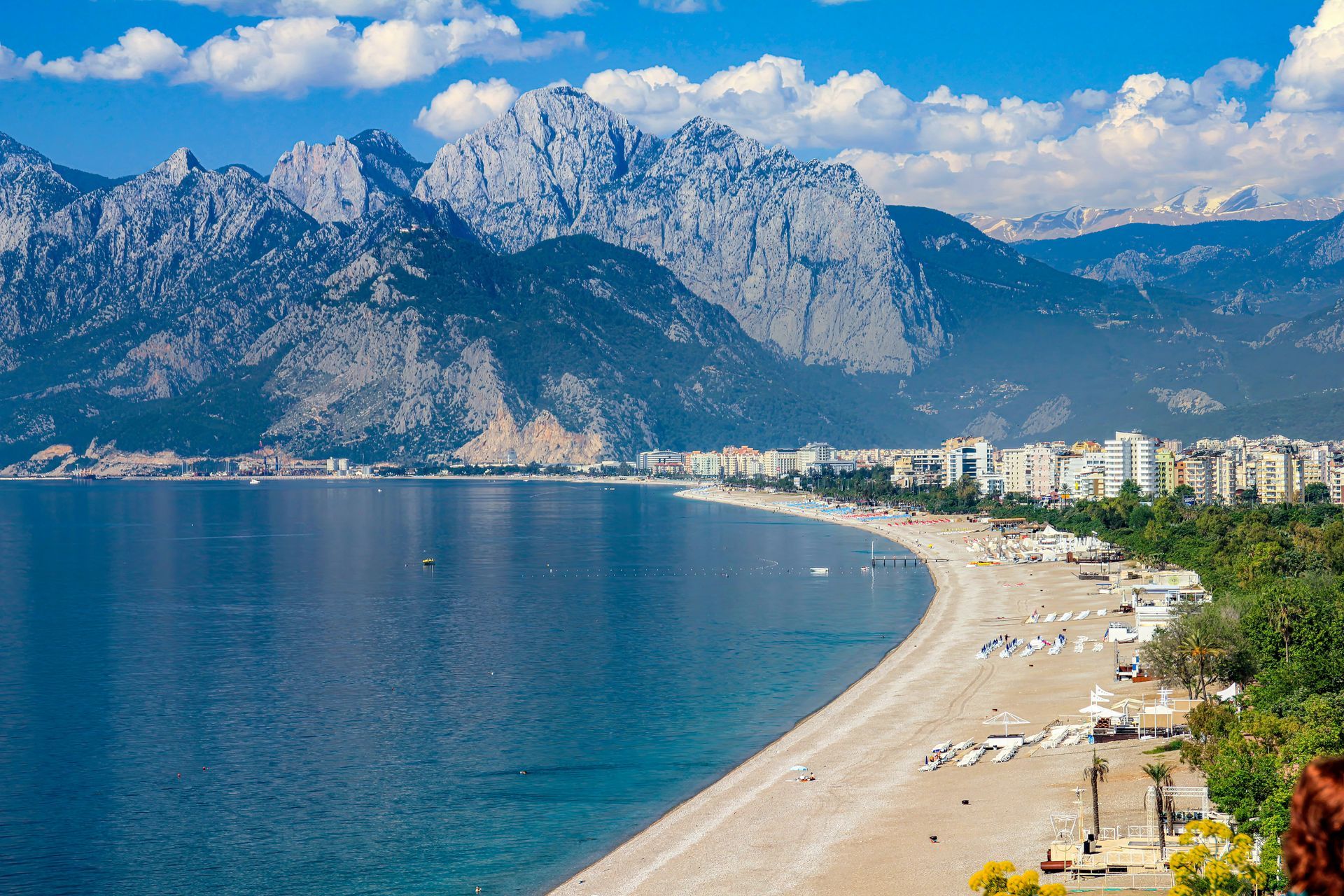 Beach with buildings, palm trees, and mountains in Antalya, Turkey.