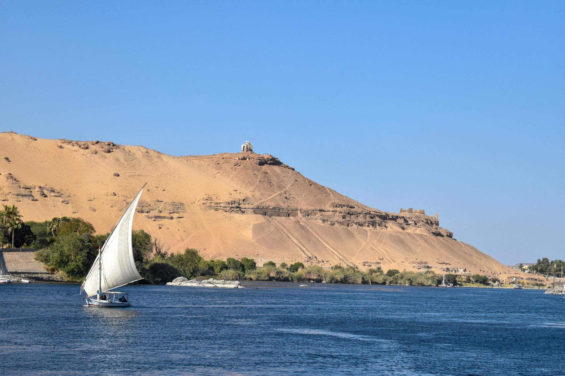 A sailboat is floating on a river with a sand dune in the background in Aswan, Egypt.