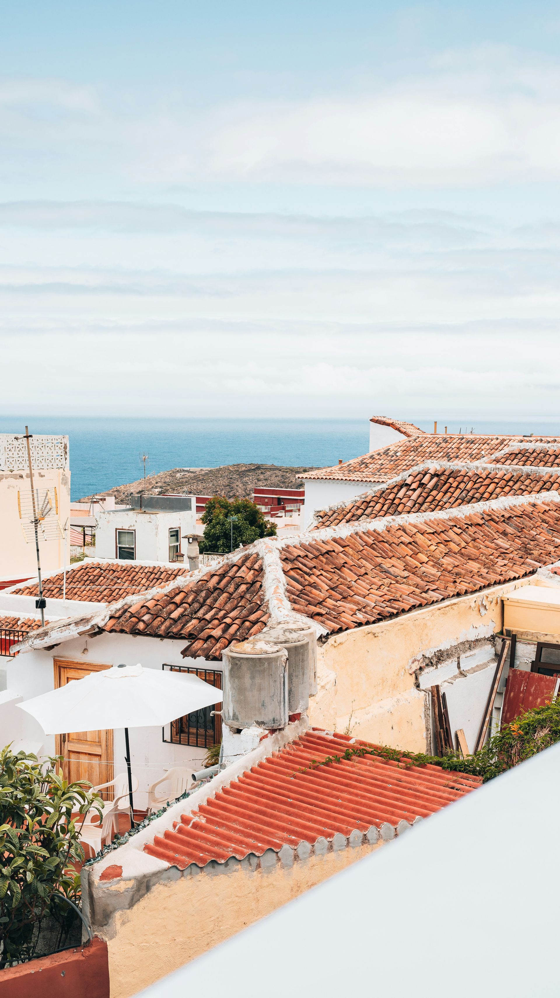 White buildings with red tile roofs overlook the blue sea under a clear sky on the Canary Islands, Spain.