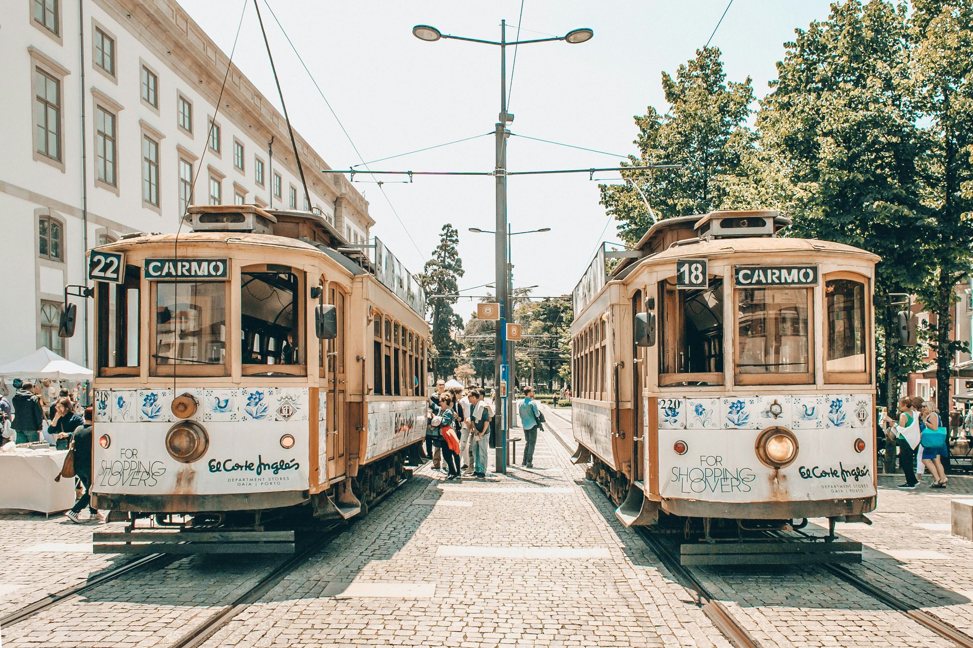 Two vintage trams parked on cobblestone tracks; passengers board in Porto, Portugal.