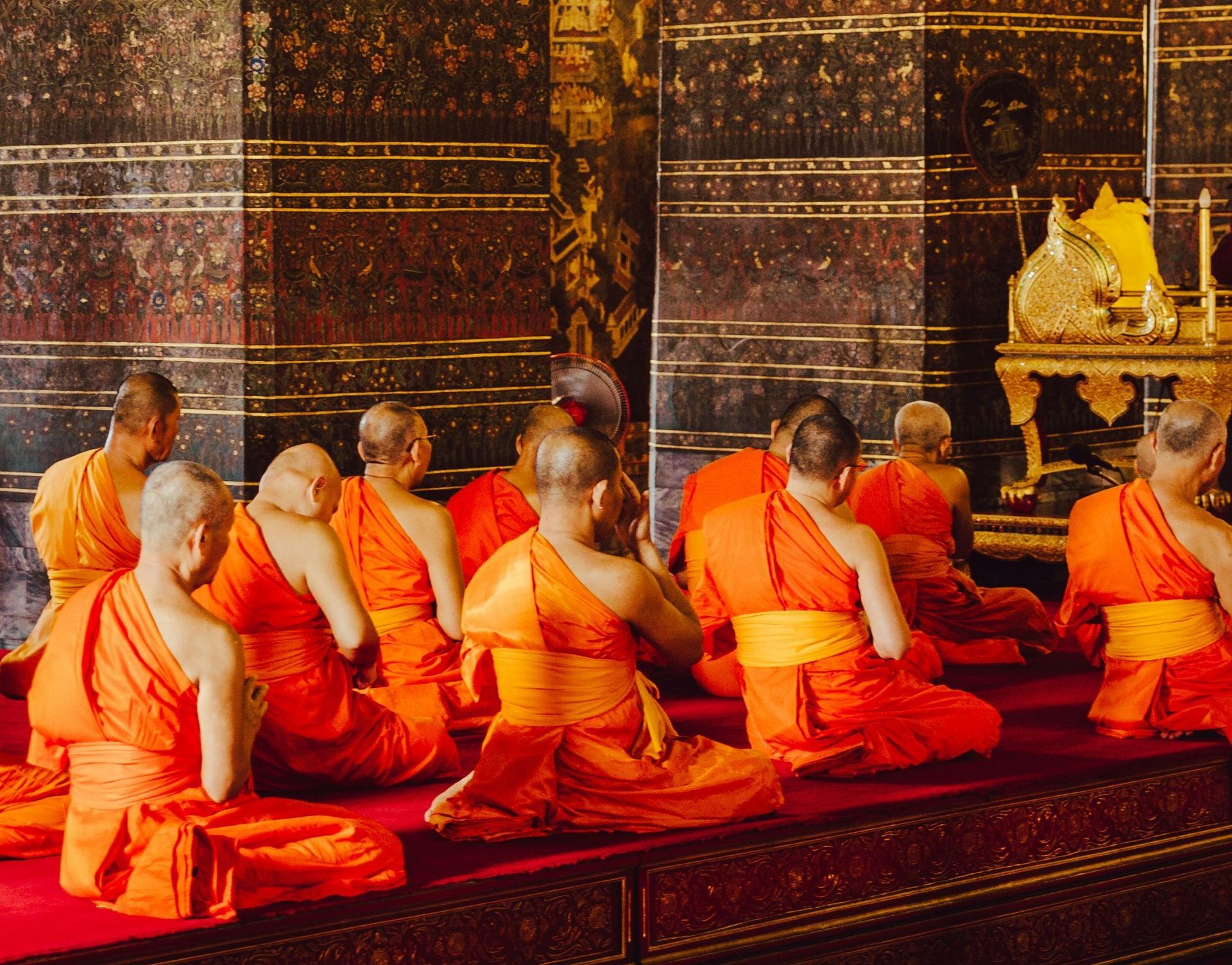 A group of monks are sitting on the floor in a temple in Thailand.