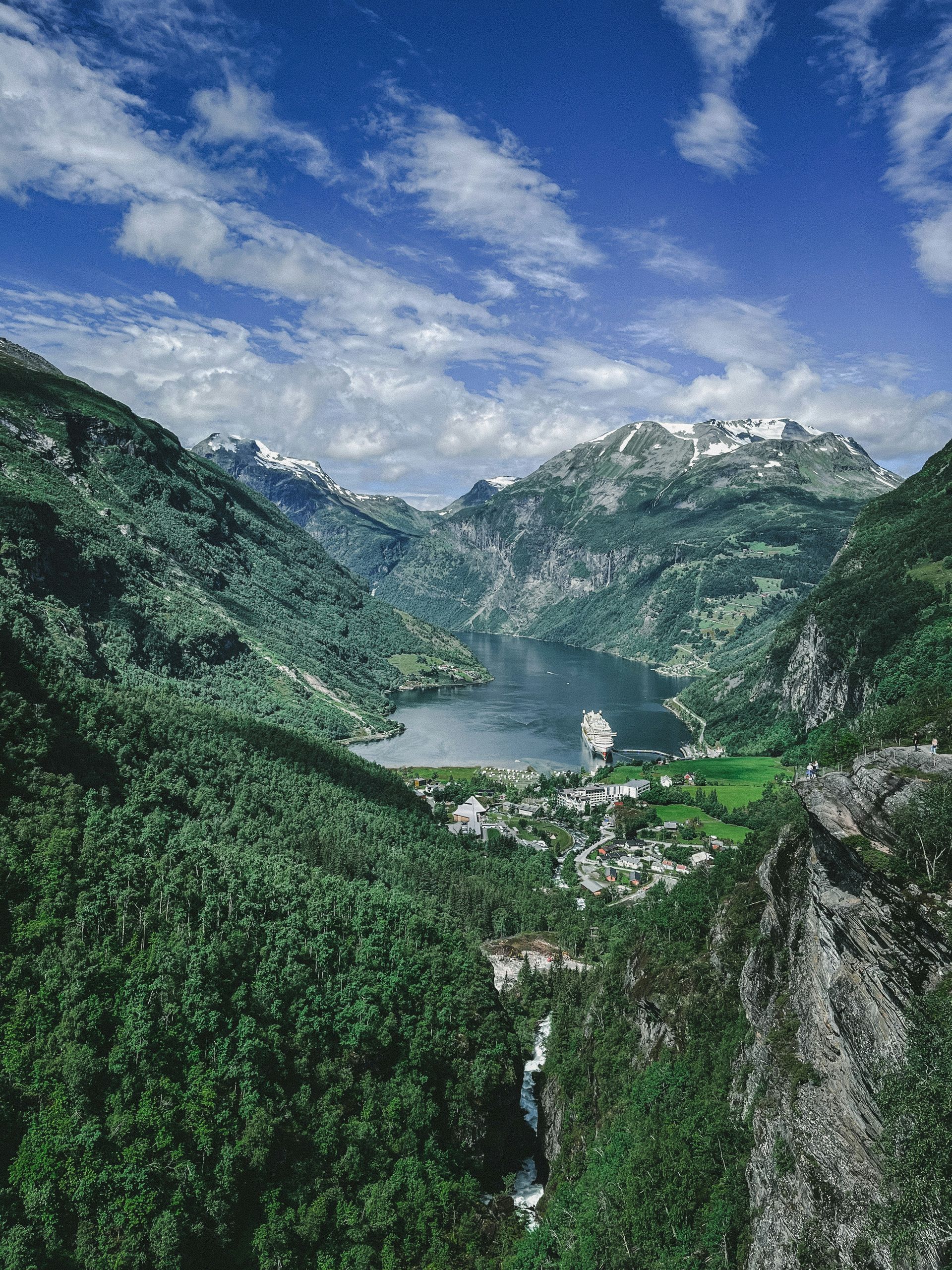 Lush green valley on the Geirangerfjord, town, and cruise ship, mountains in the background in Norway.