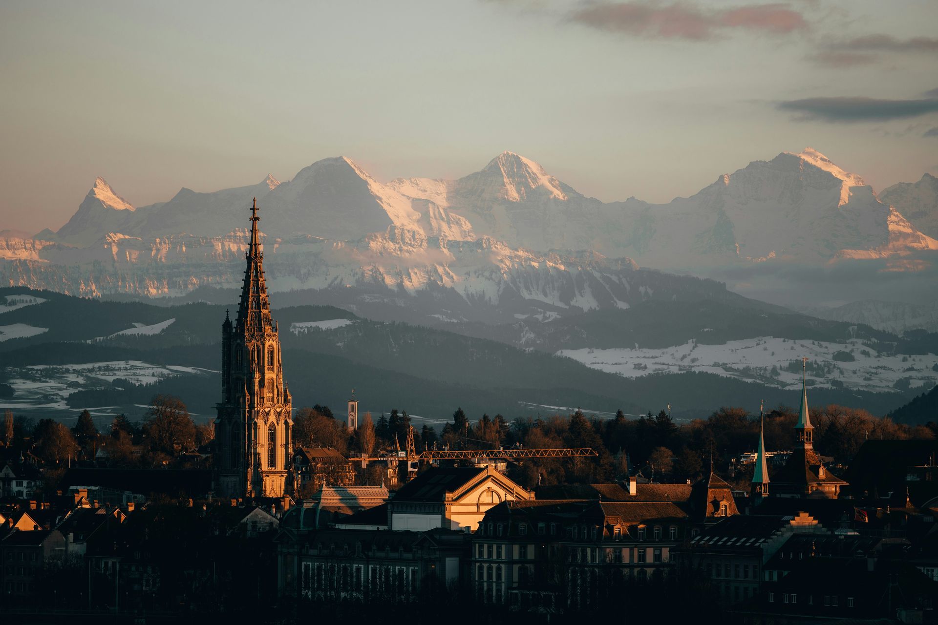 Golden hour over Bern. Switzerland's skyline with a tall church spire and snow-capped mountains in the background.
