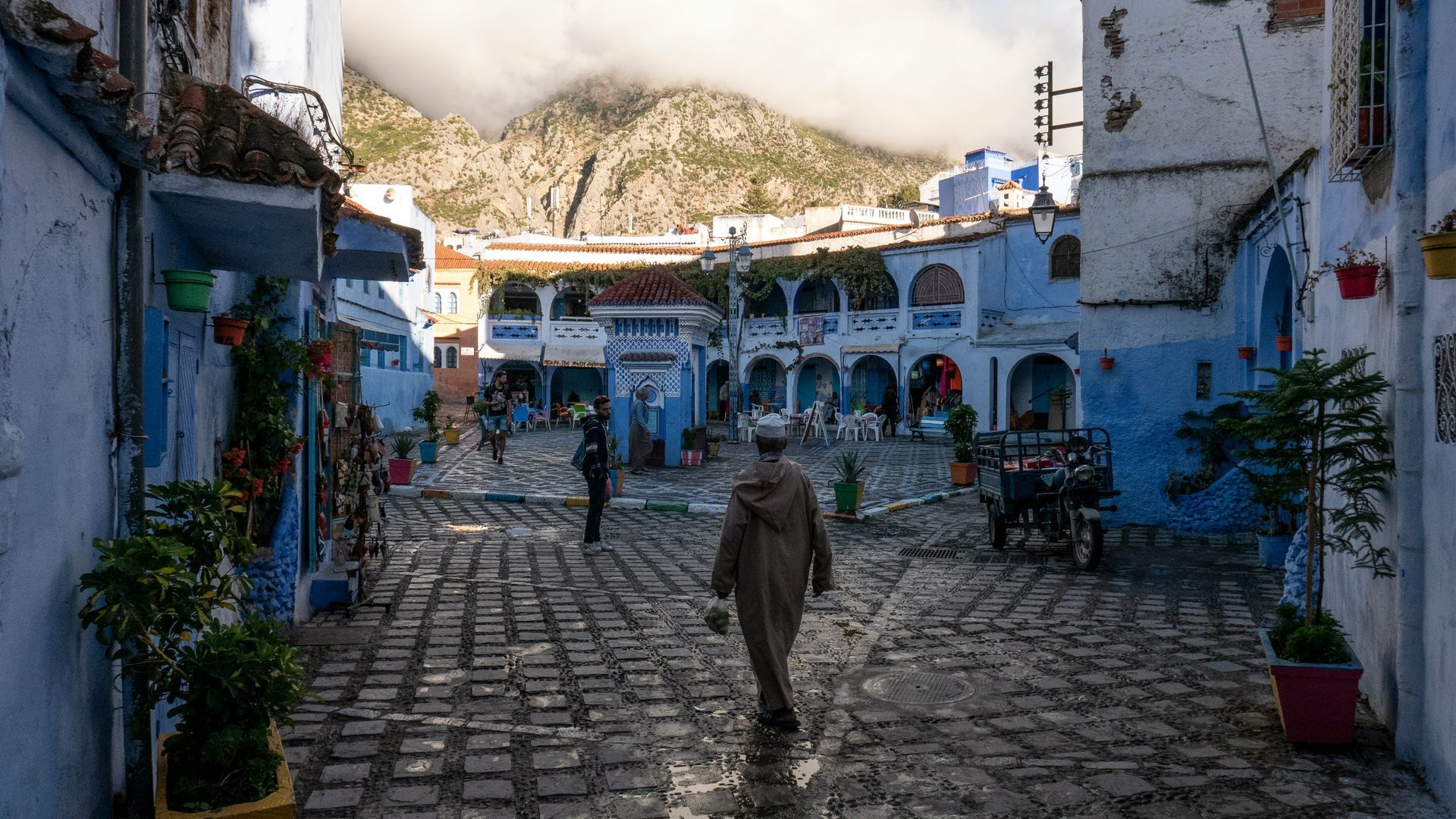 A man is walking down a cobblestone street in Chefchaouen, Morocco.