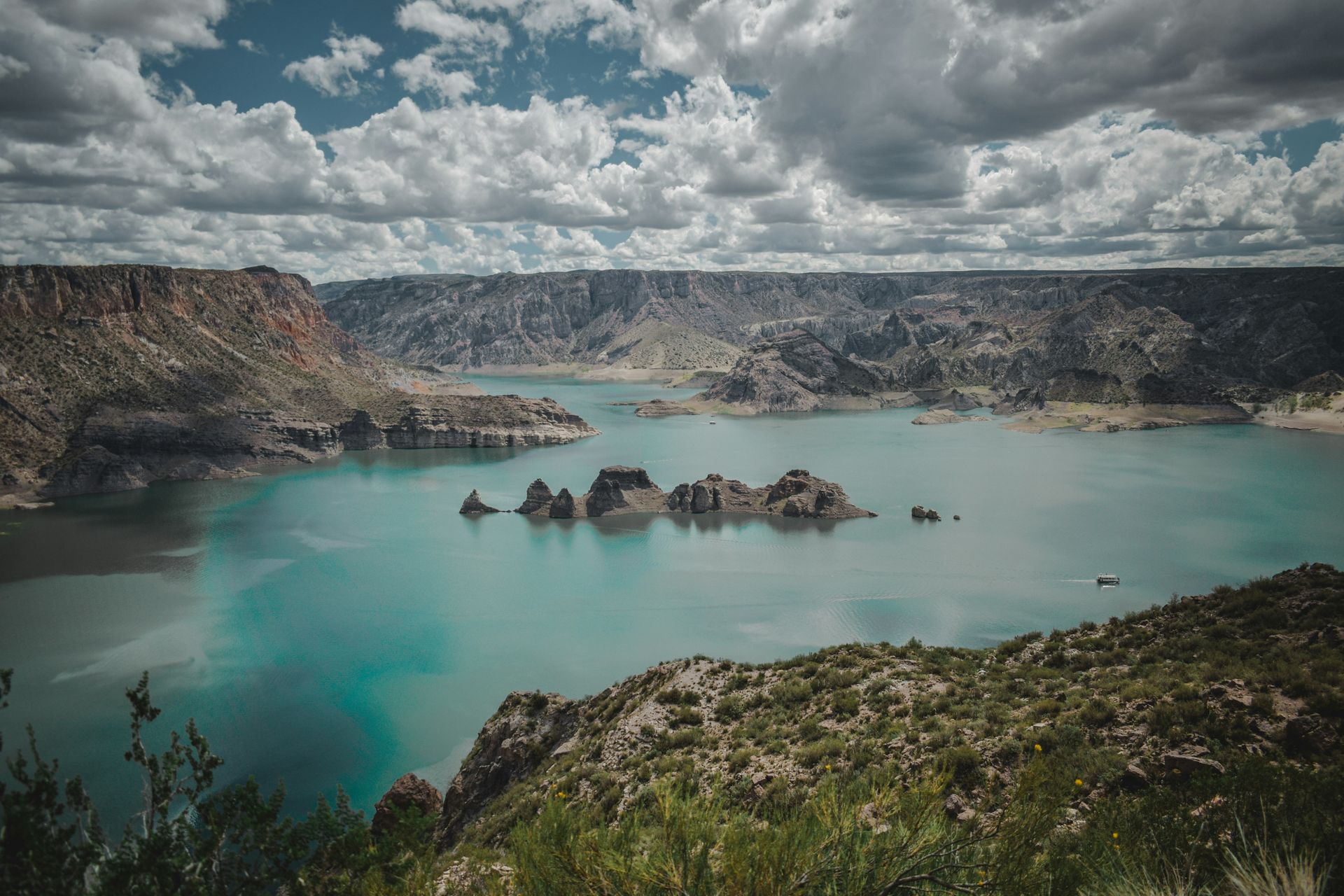 Scenic view of a turquoise lake surrounded by rocky mountains under a cloudy sky in Mendoza, Argentina.