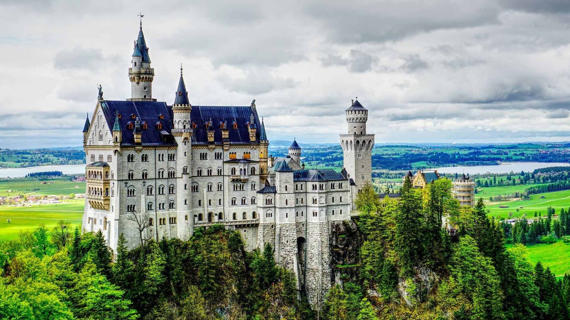 Neuschwanstein Castle, Bavaria, Germany, white castle on hilltop, surrounded by green trees, overlooking lakes and landscape.