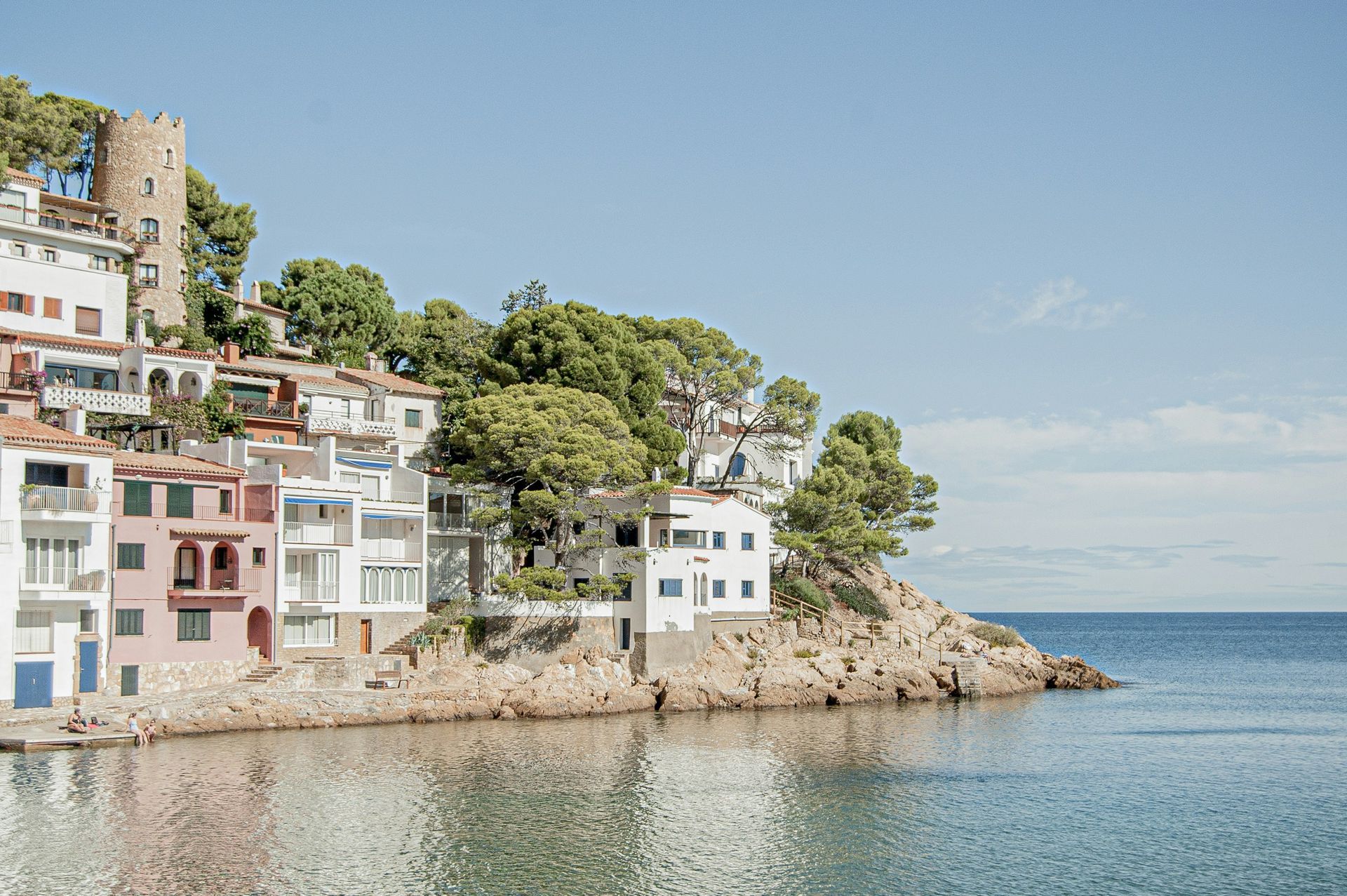 Coastal village with colorful buildings perched on a cliff overlooking the calm blue sea in Costa Brava, Spain.
