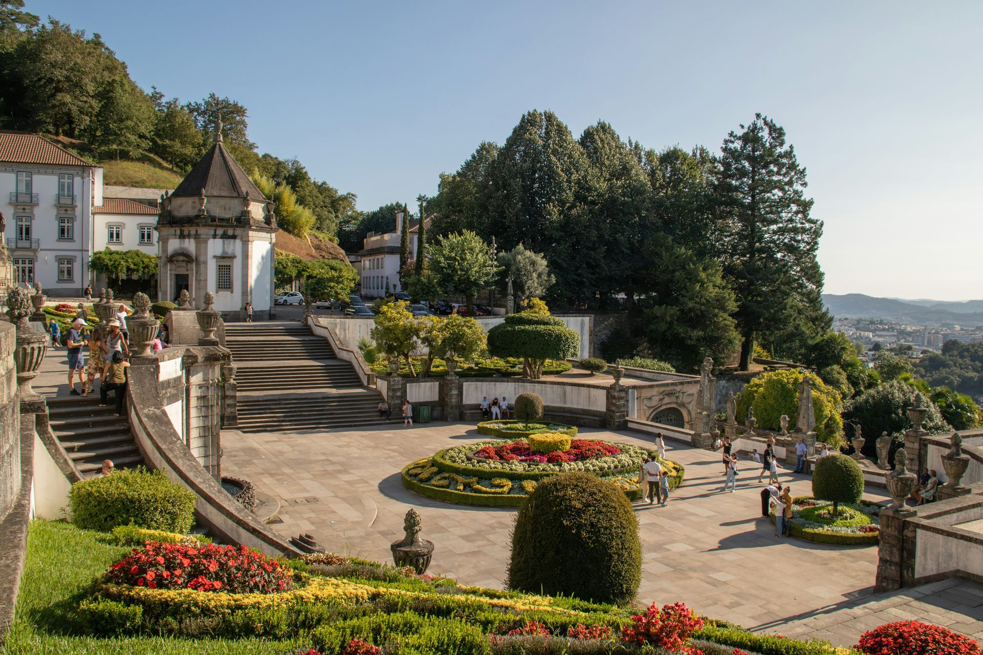 A tiered garden with ornate stonework, flower beds, and a chapel on a hillside in Braga, Portugal.