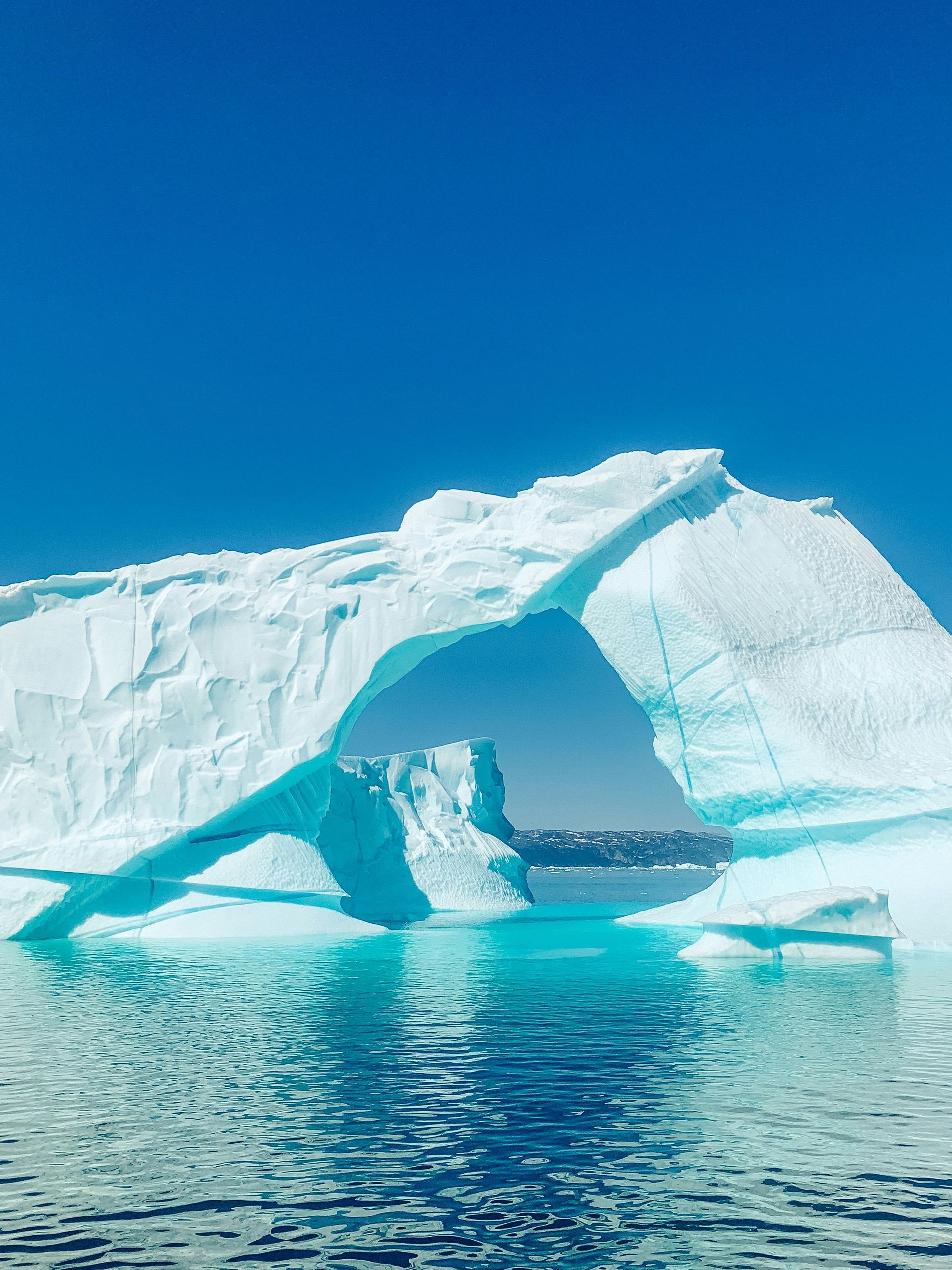 Iceberg with arch formation over blue water, bright blue sky in Disko Bay, Greenland.