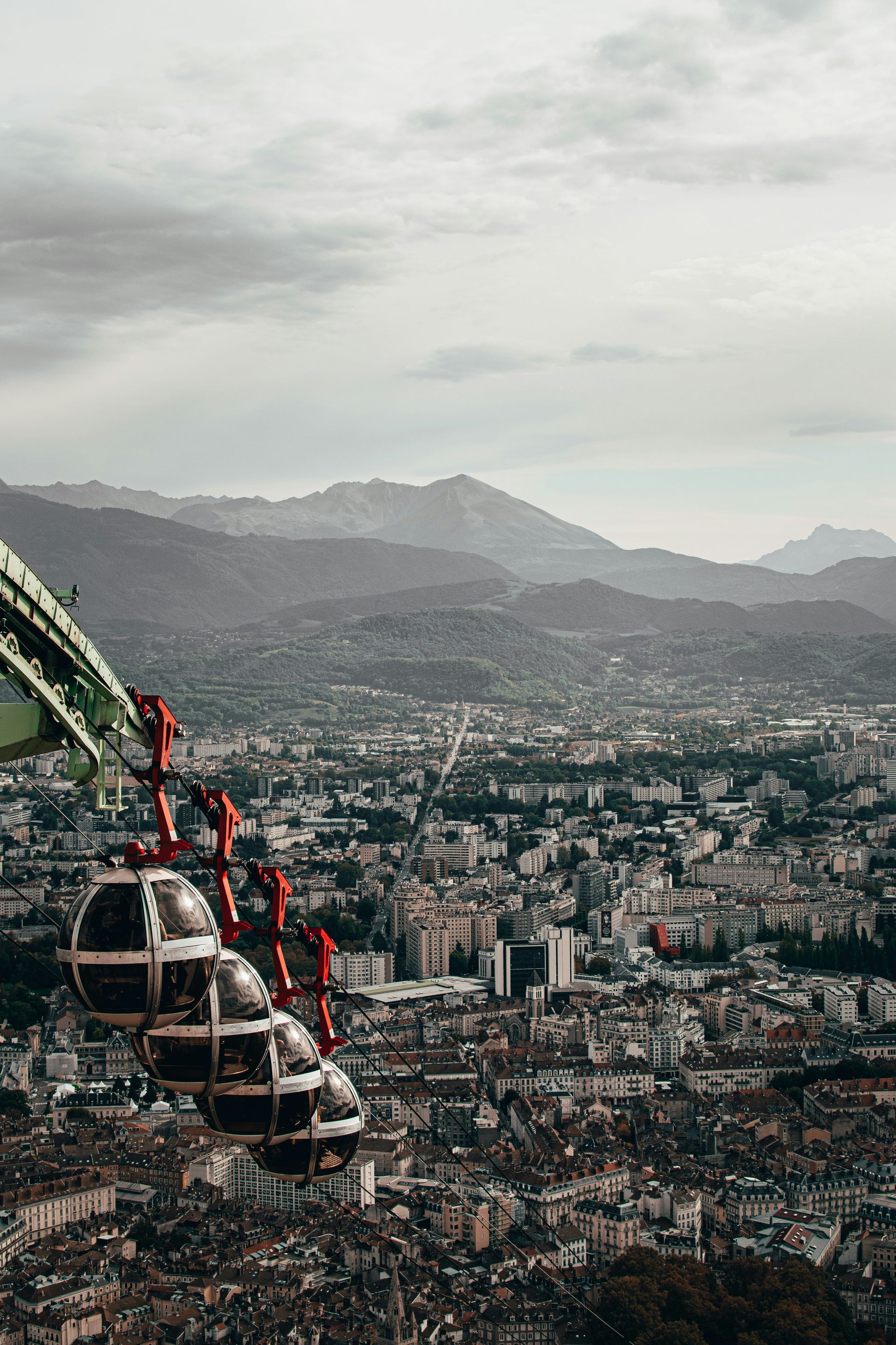 A cable car is going over Grenoble, France with mountains in the background.