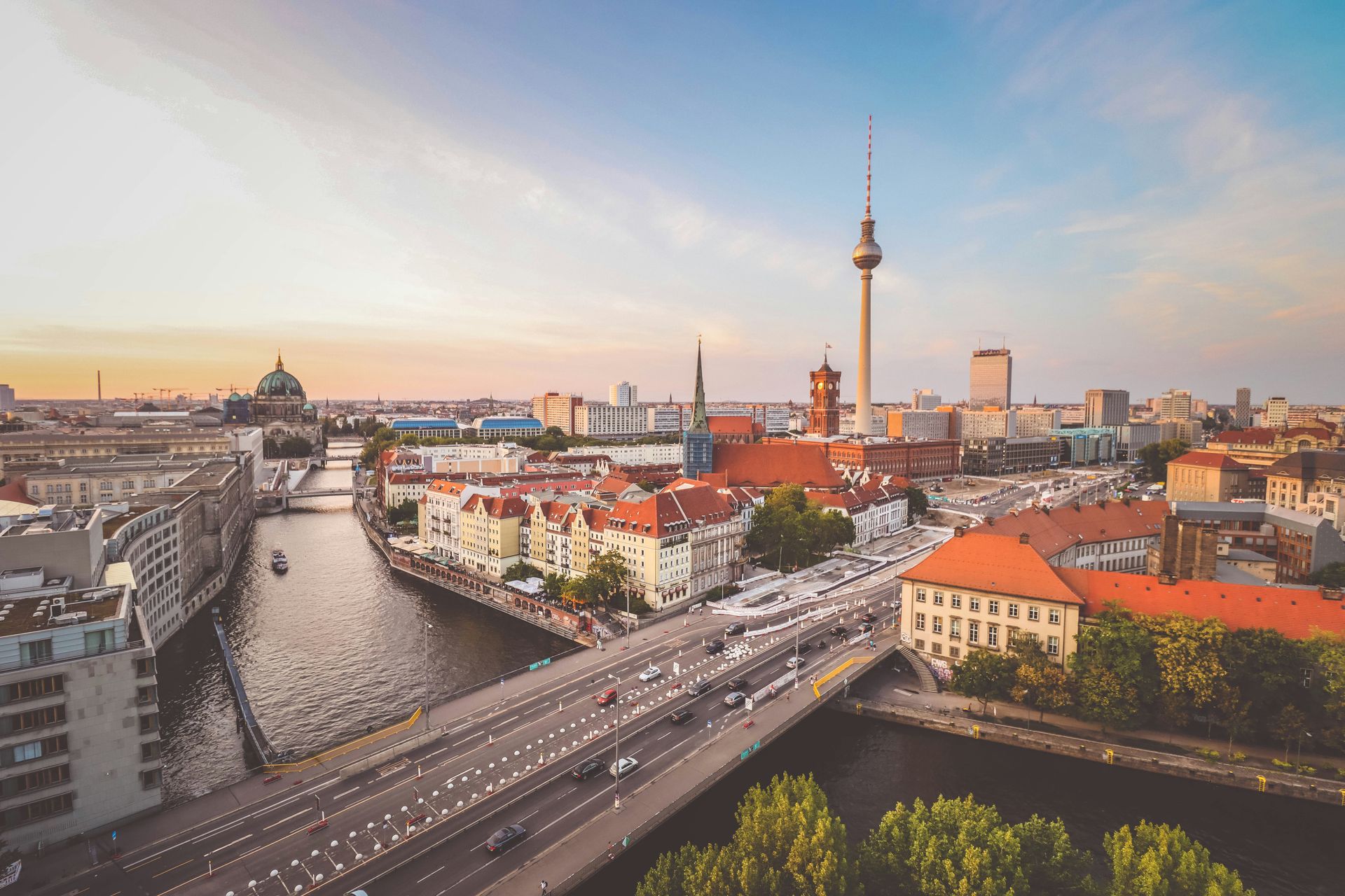 Berlin skyline at sunset, featuring Spree River, Fernsehturm TV tower, and historic buildings.
