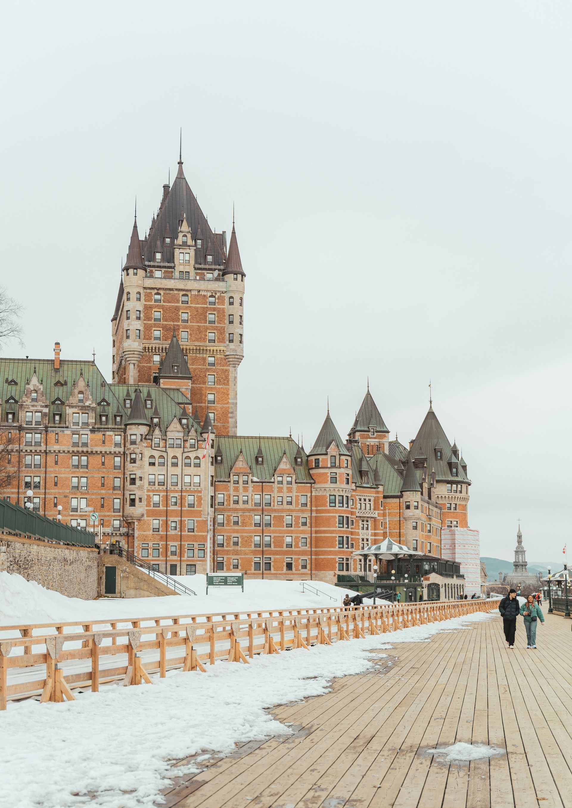 Château Frontenac in Quebec City, Canada, a large brown and green castle-like building with a wooden walkway and snow in the foreground.