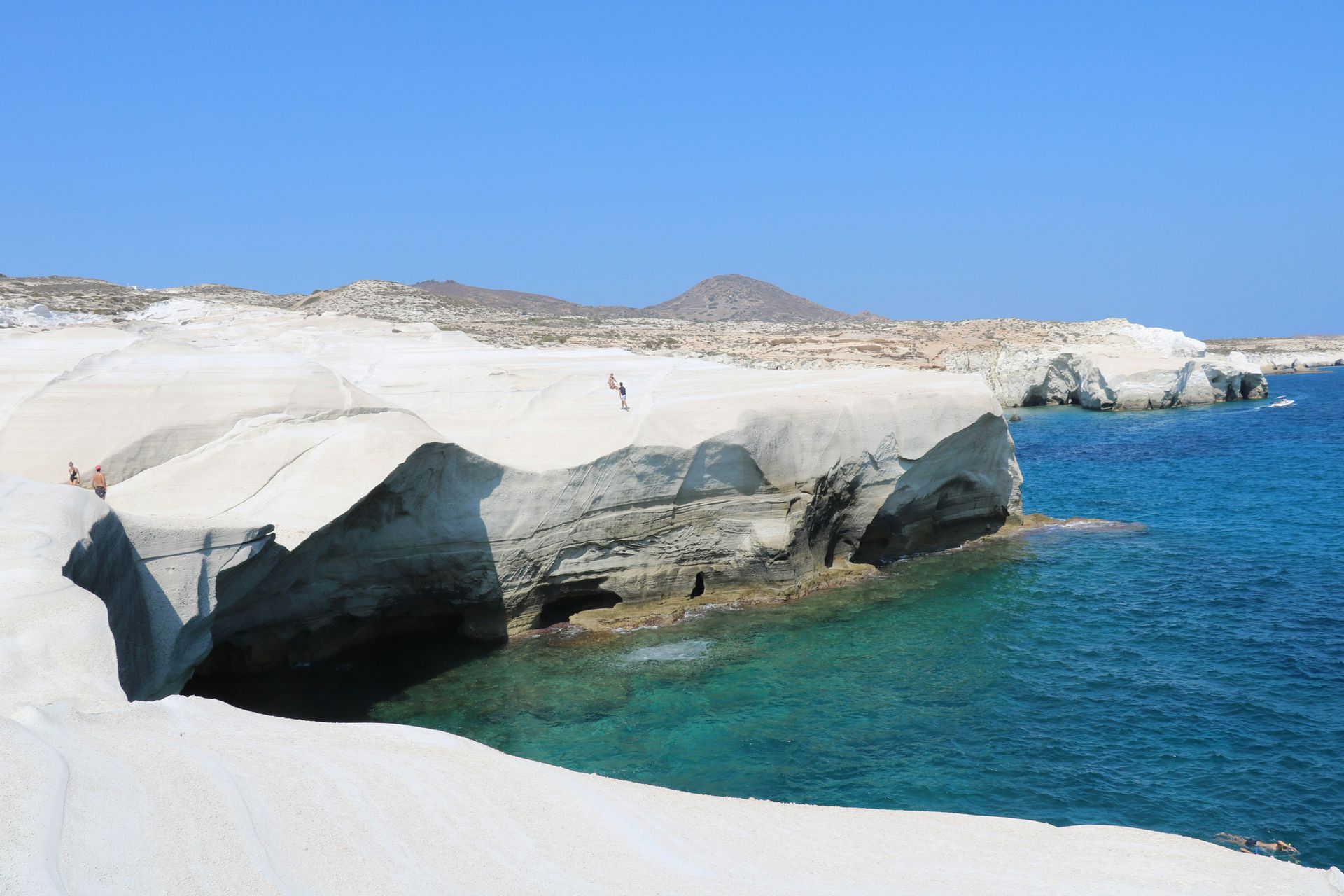 A cliff overlooking a body of water with mountains in the background in Milos, Greece.