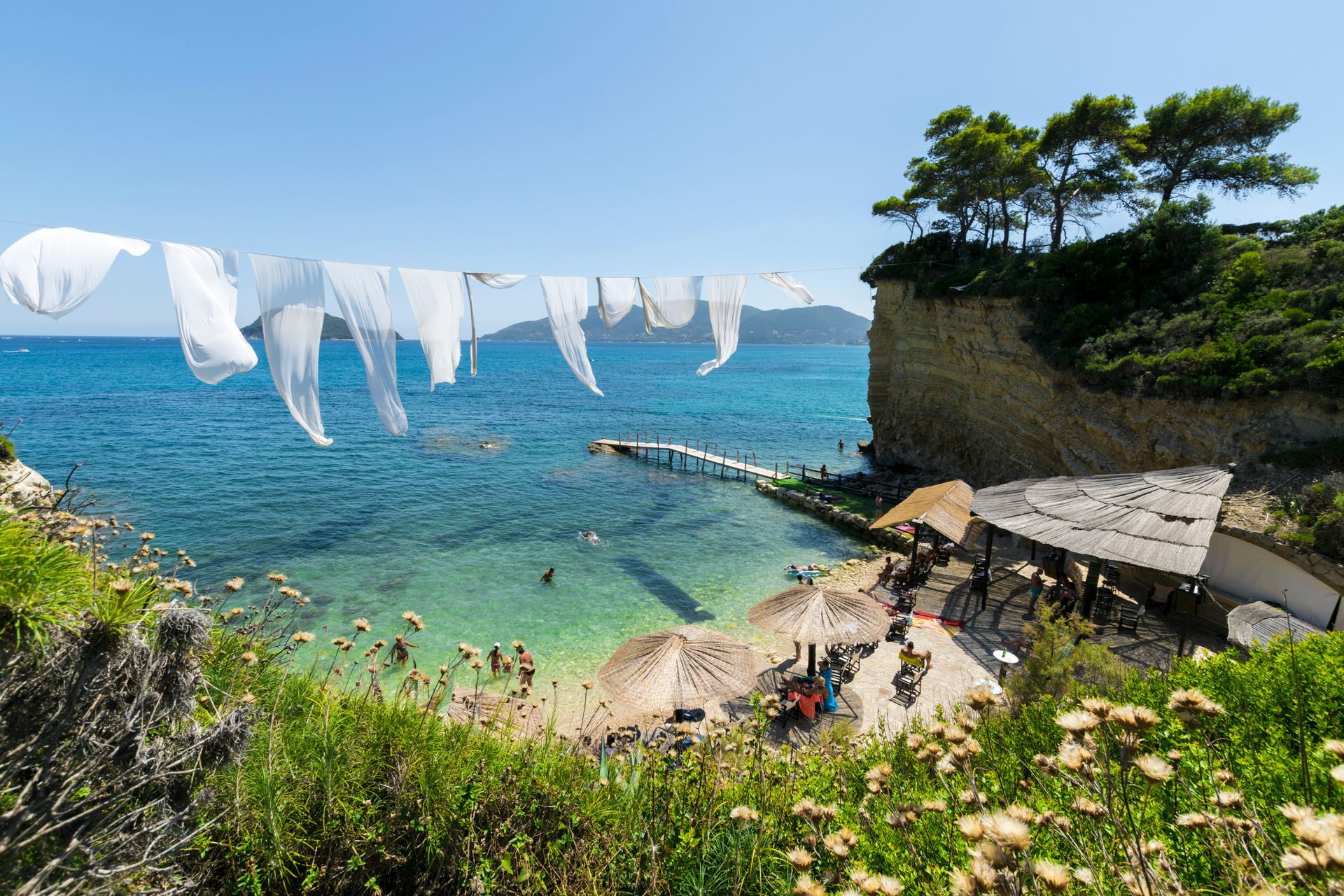 A row of white clothes hanging on a clothes line overlooking a beach in Zakynthos, Greece.