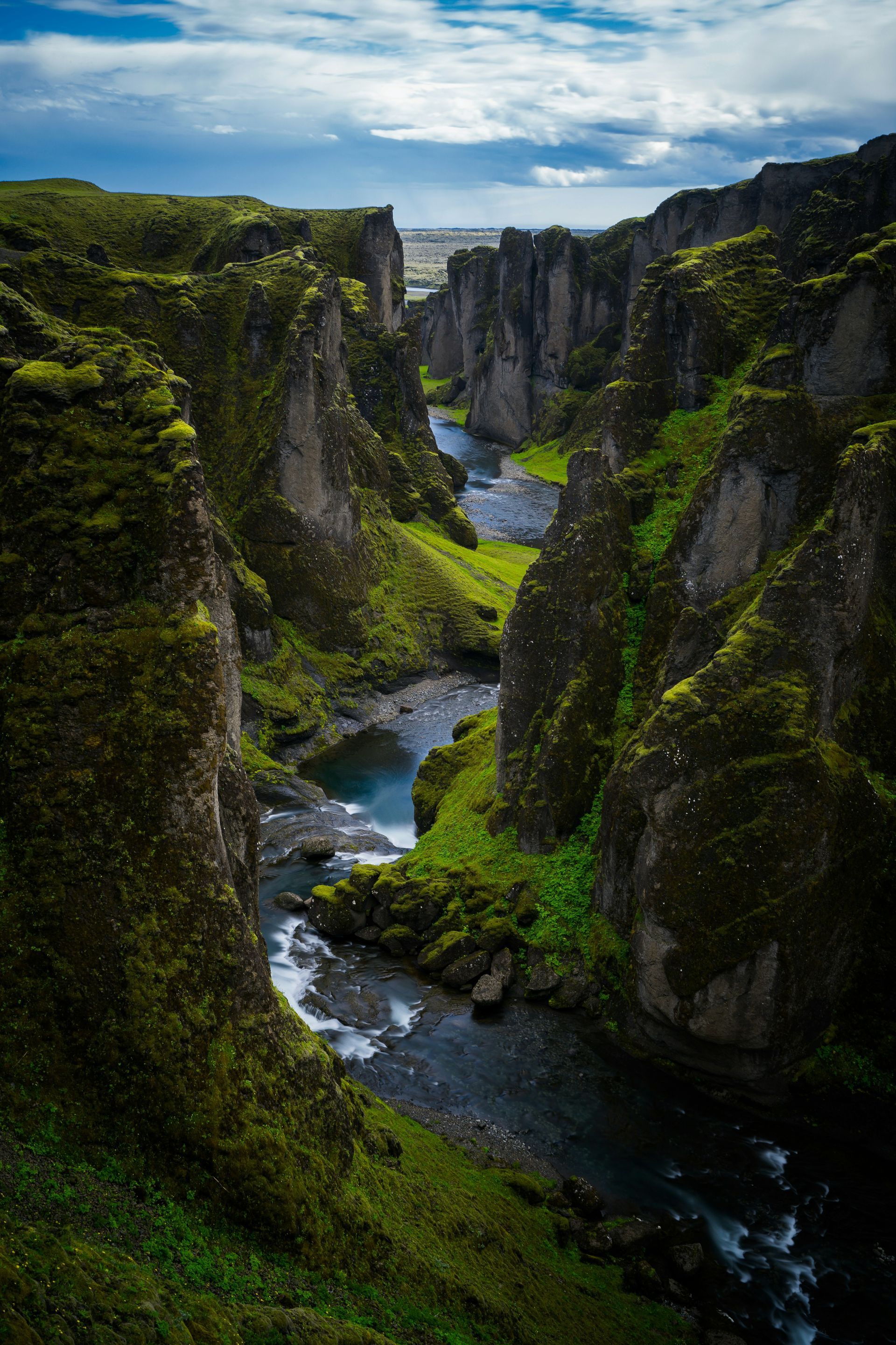 River winding through a deep, mossy canyon under a cloudy sky at Fjaðrárgljúfur, Iceland.