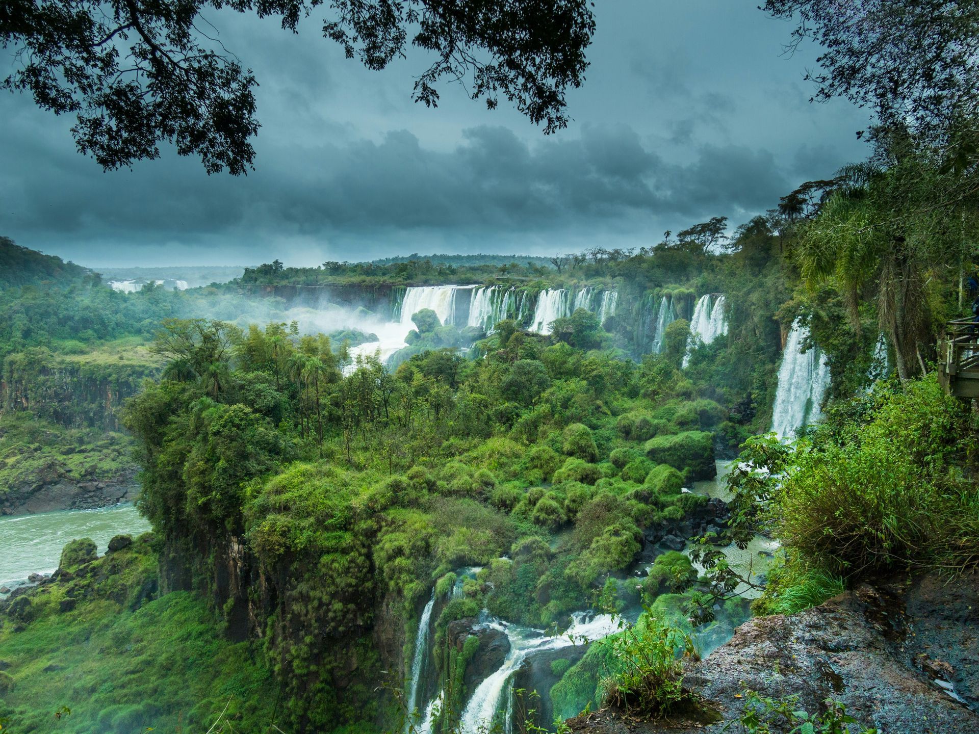 Lush green landscape with multiple waterfalls cascading over cliffs, mist rising at Iguazu Falls, Argentina.