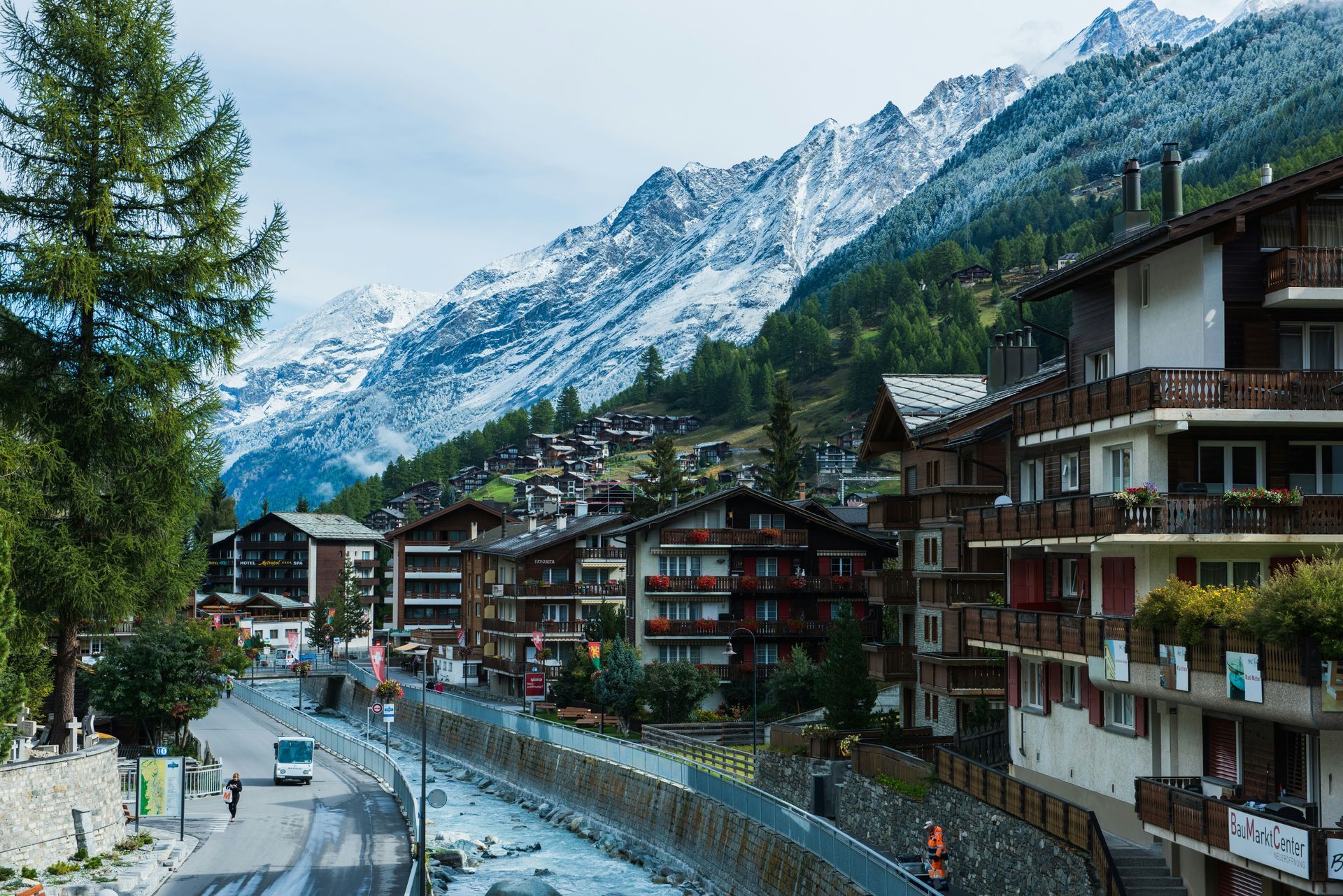 A Swiss village nestled in a valley, with buildings, a river, and snowy mountains in the background in Zermatt, Switzerland.