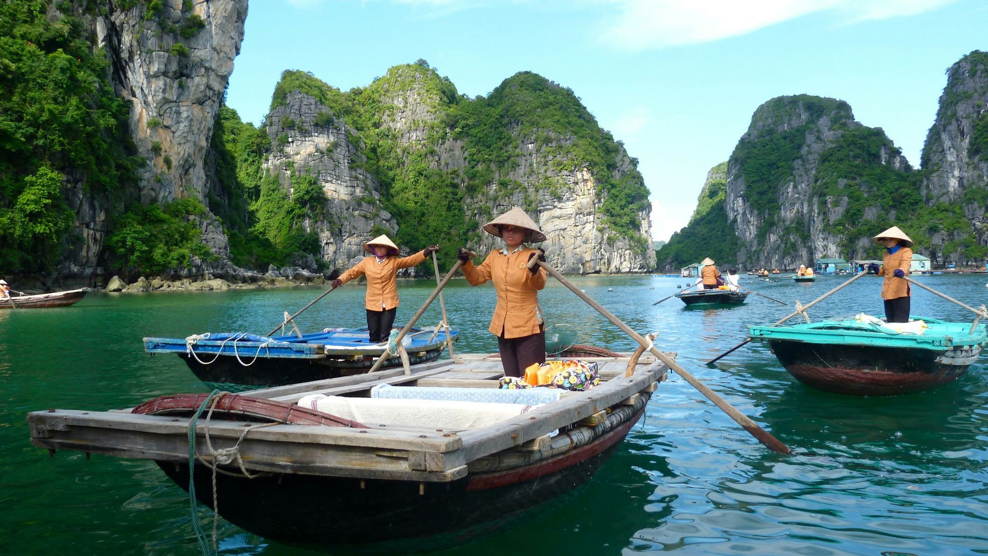 Boats with women rowing in Ha Long Bay, Vietnam, amidst limestone cliffs and green water.