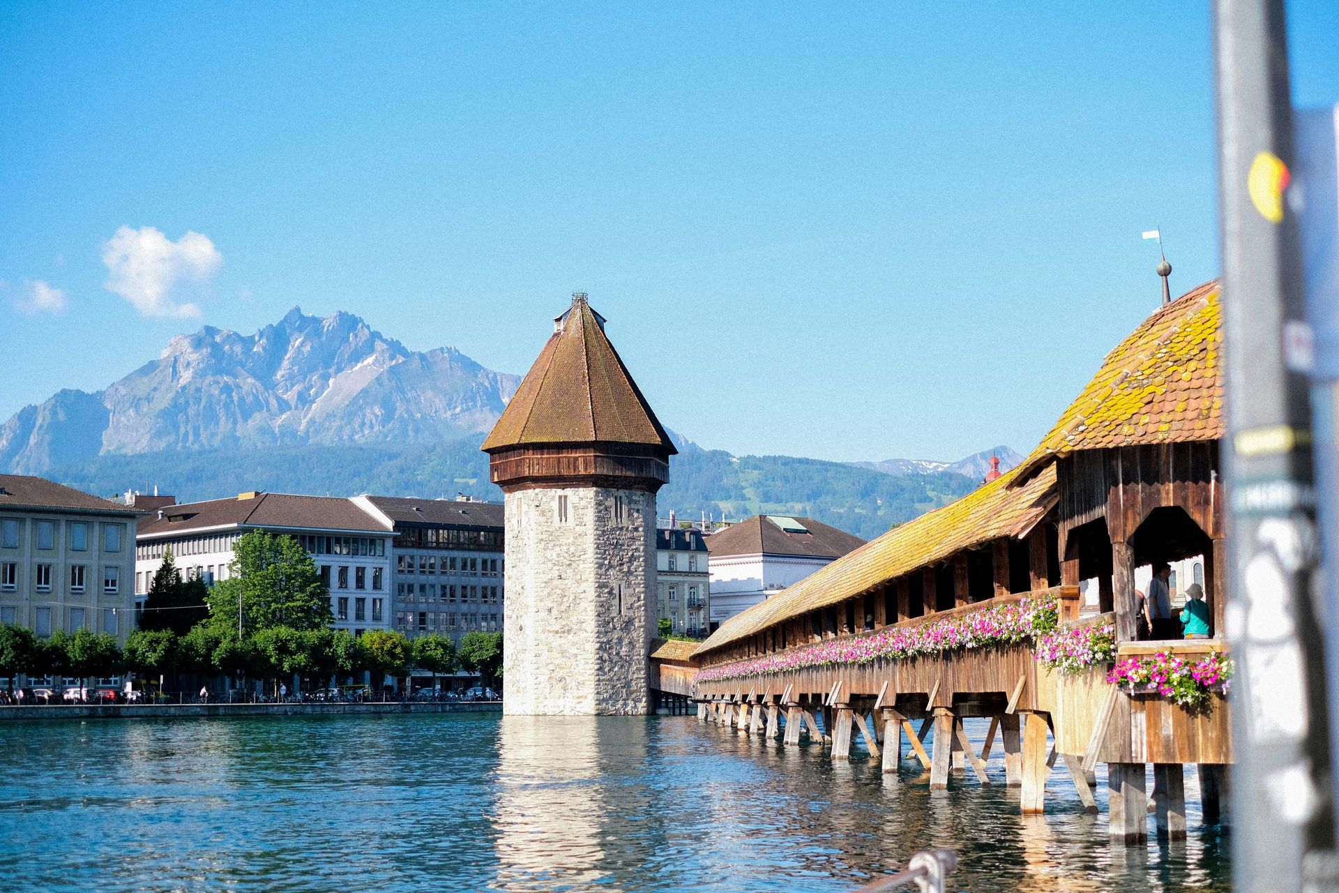Wooden bridge with tower on a lake, mountain backdrop in Lucerne, Switzerland.