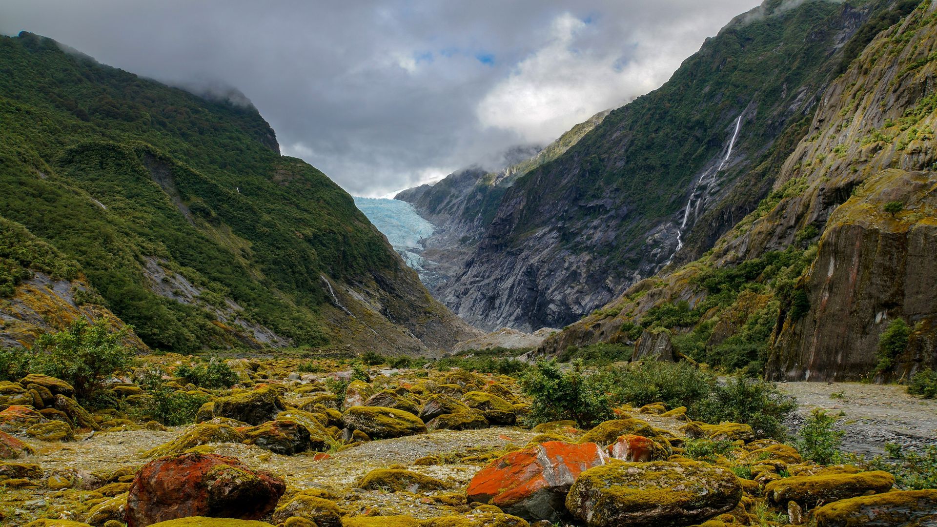 A frozen river glacier runs through a valley between two mountains at the Franz Josef Glacier in New Zealand.