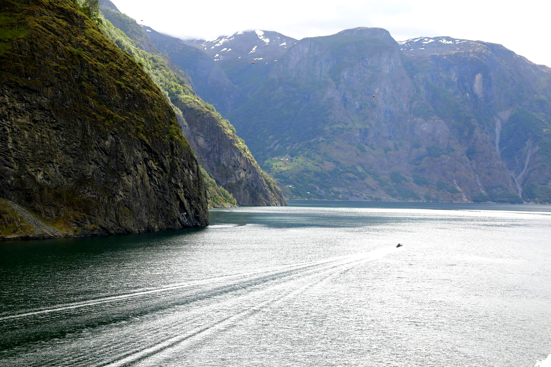 Sognefjord with dark cliffs, calm water, and distant mountains under a bright sky in Norway.