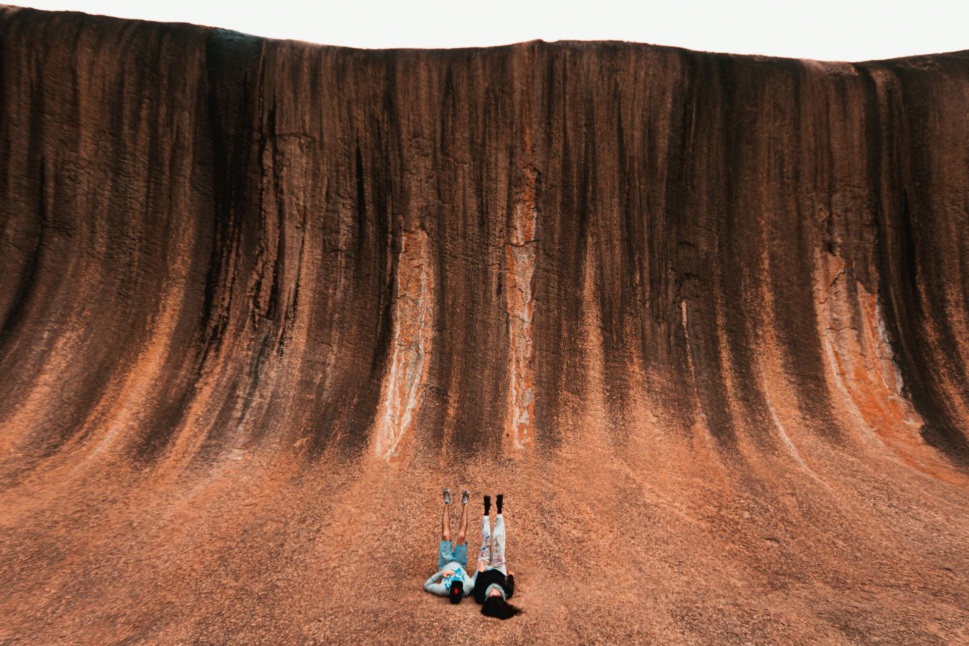 A couple of people are sitting on the ground in front of a large rock formation in Western Australia.