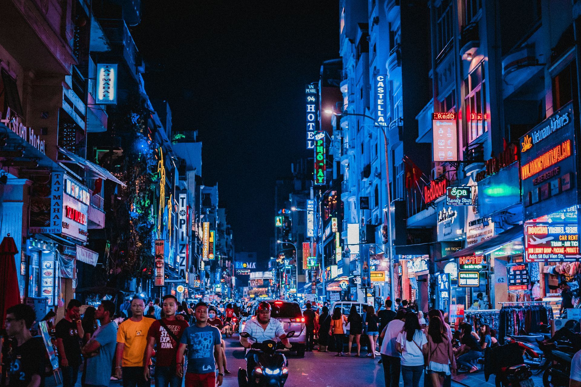 Nighttime street scene in Ho Chi Minh, Vietnam, featuring brightly lit signs, pedestrians, and motorbikes.