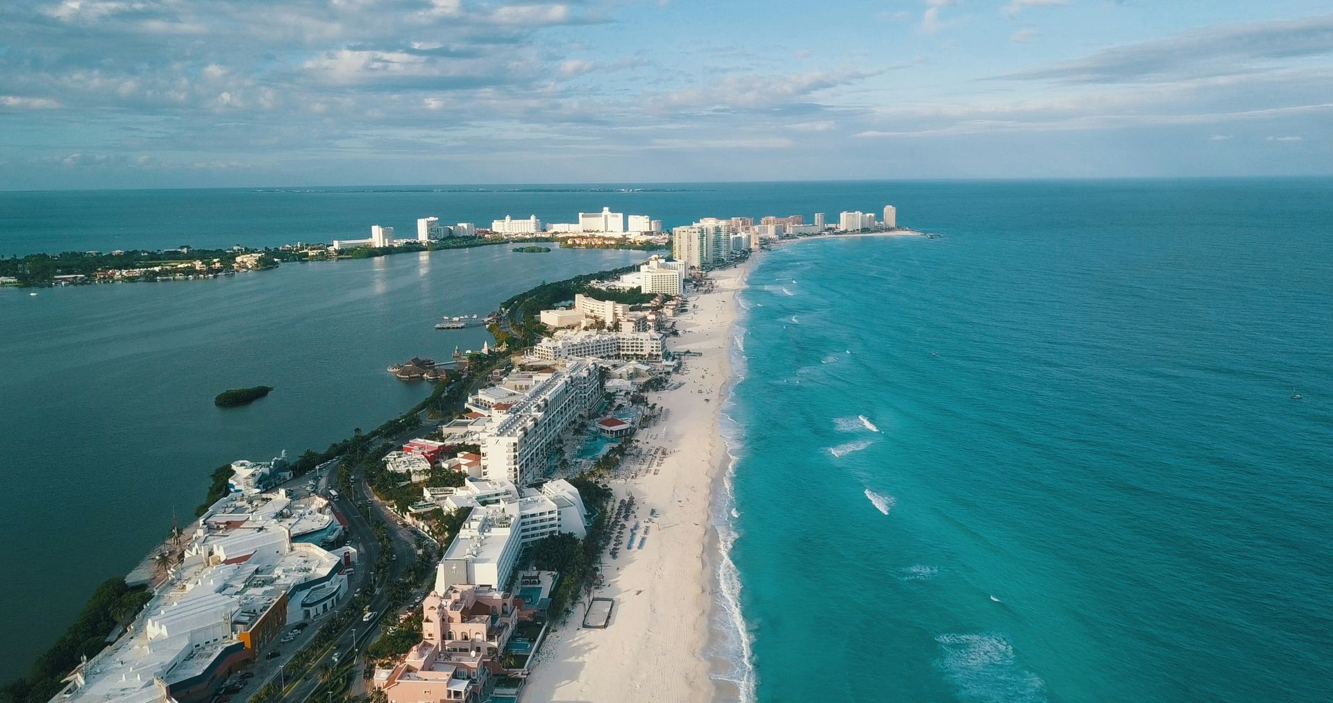 Aerial view of a beach in Cancun, Mexico. Turquoise ocean water meets white sand and a strip of hotels and buildings.