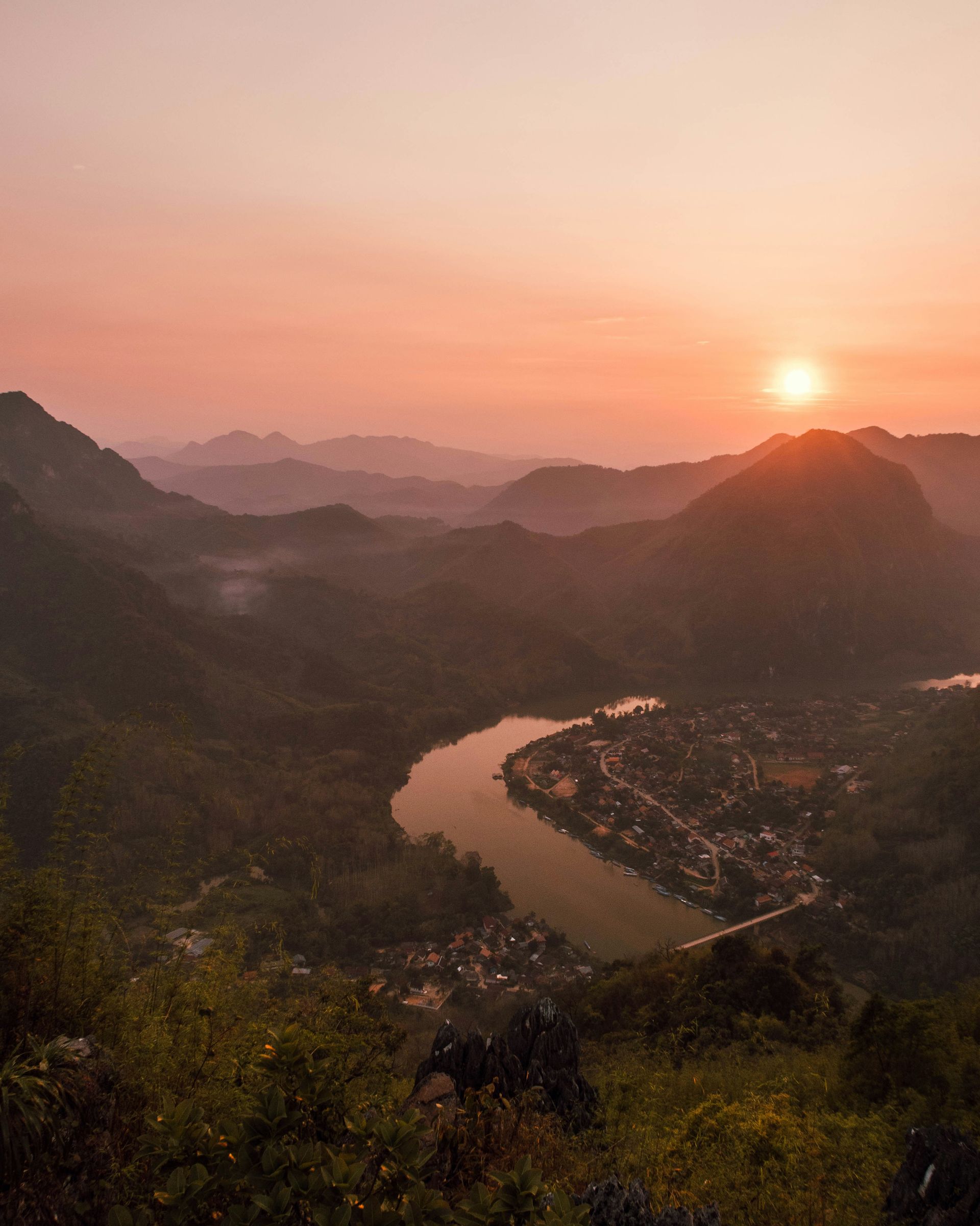 Sunset over misty mountains and river, with village below in Nong Khiaw, Laos.