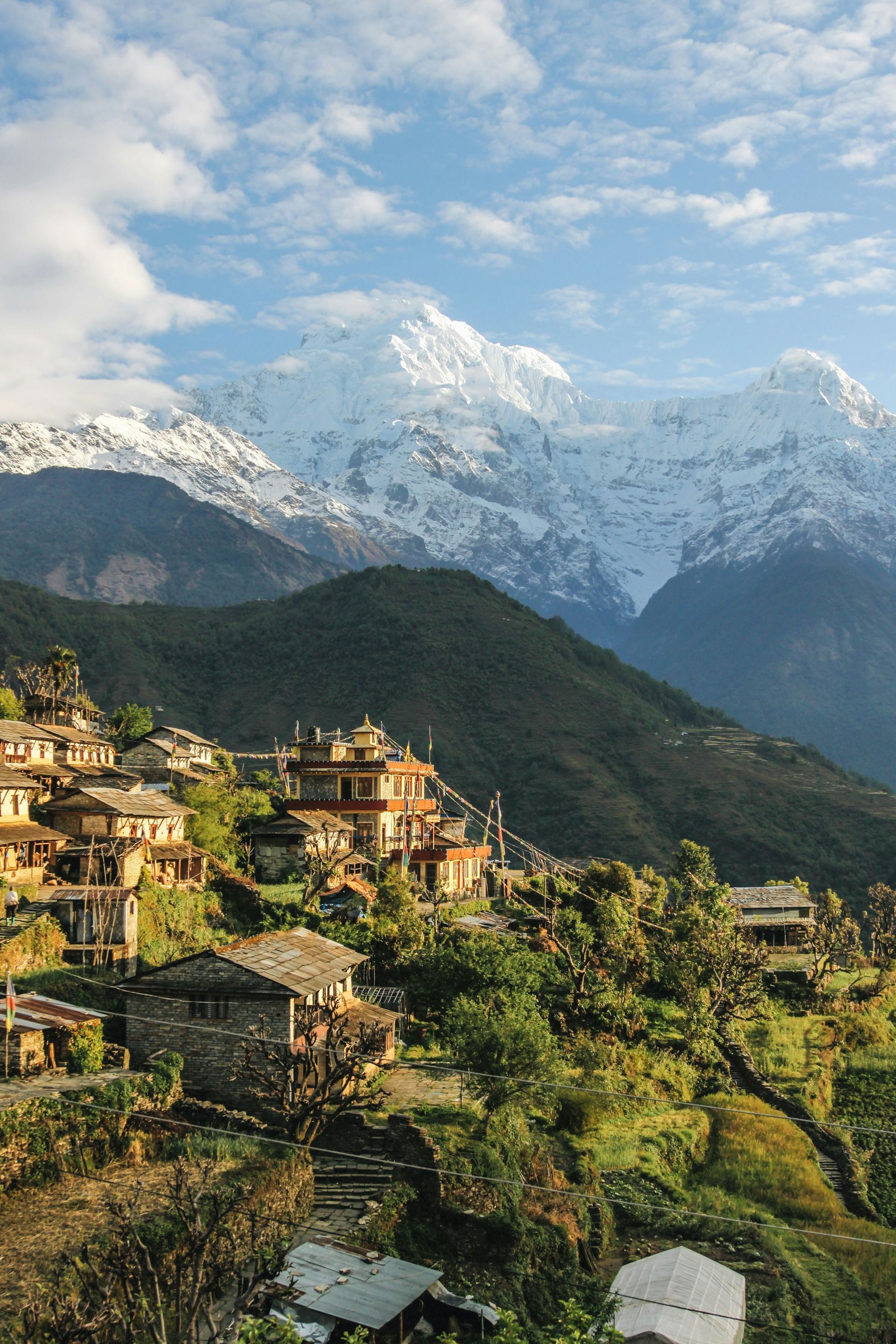 Village nestled on a mountainside, with snowy peaks in the background, in Annapurna, Nepal.
