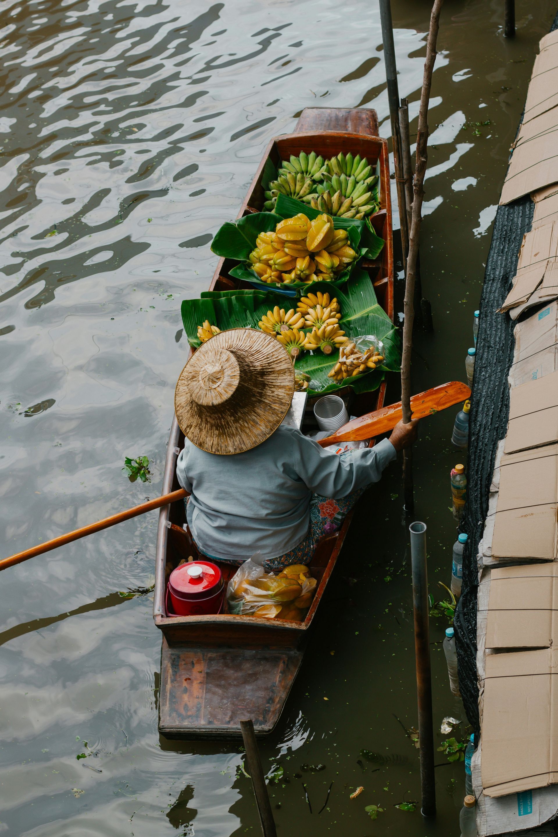 A man in a straw hat is rowing a boat filled with bananas on the Damnoen Saduak river market in Thailand.