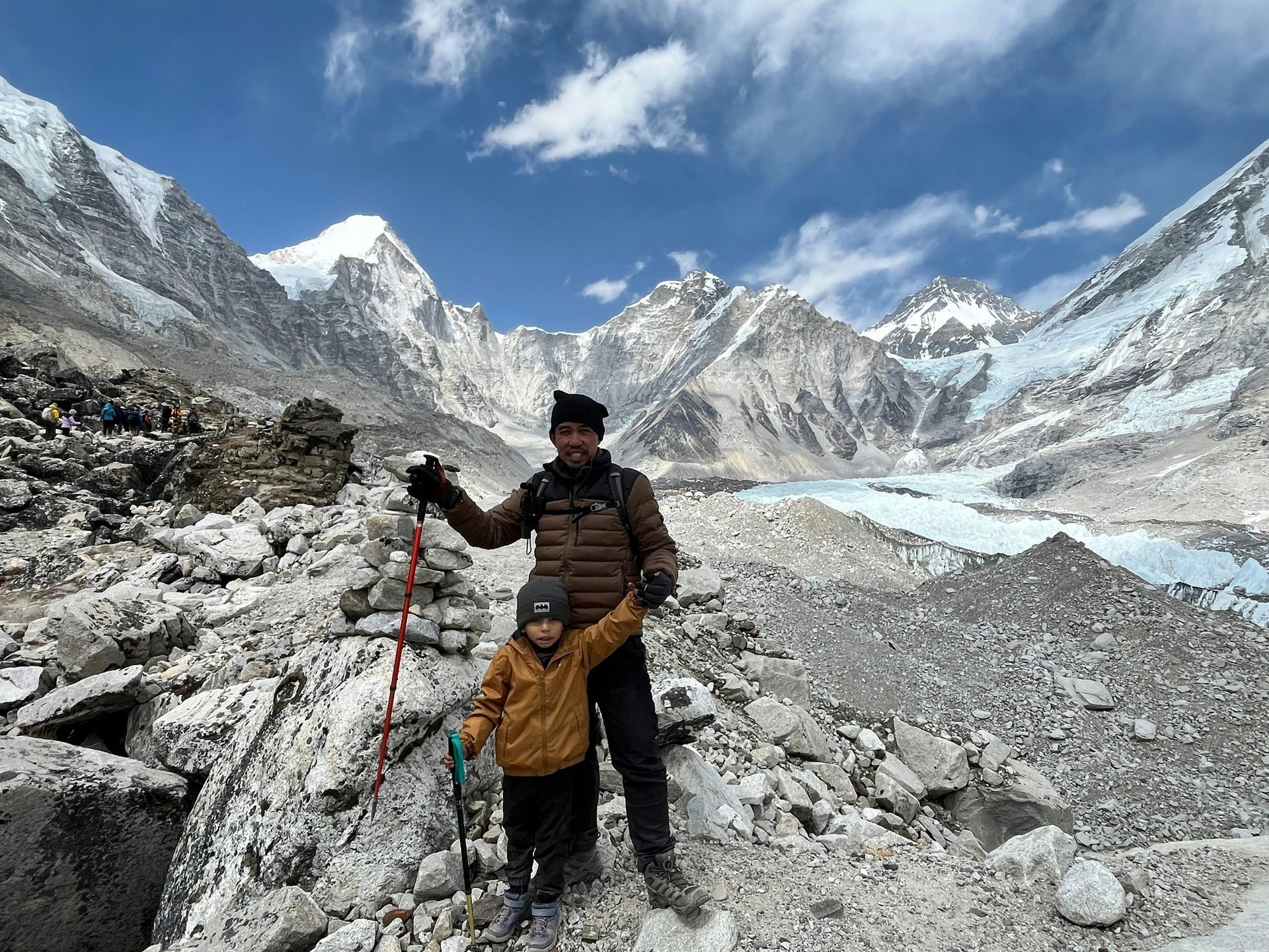 Man and child stand on rocky terrain, snow-capped mountains in Sagarmatha, Nepal.