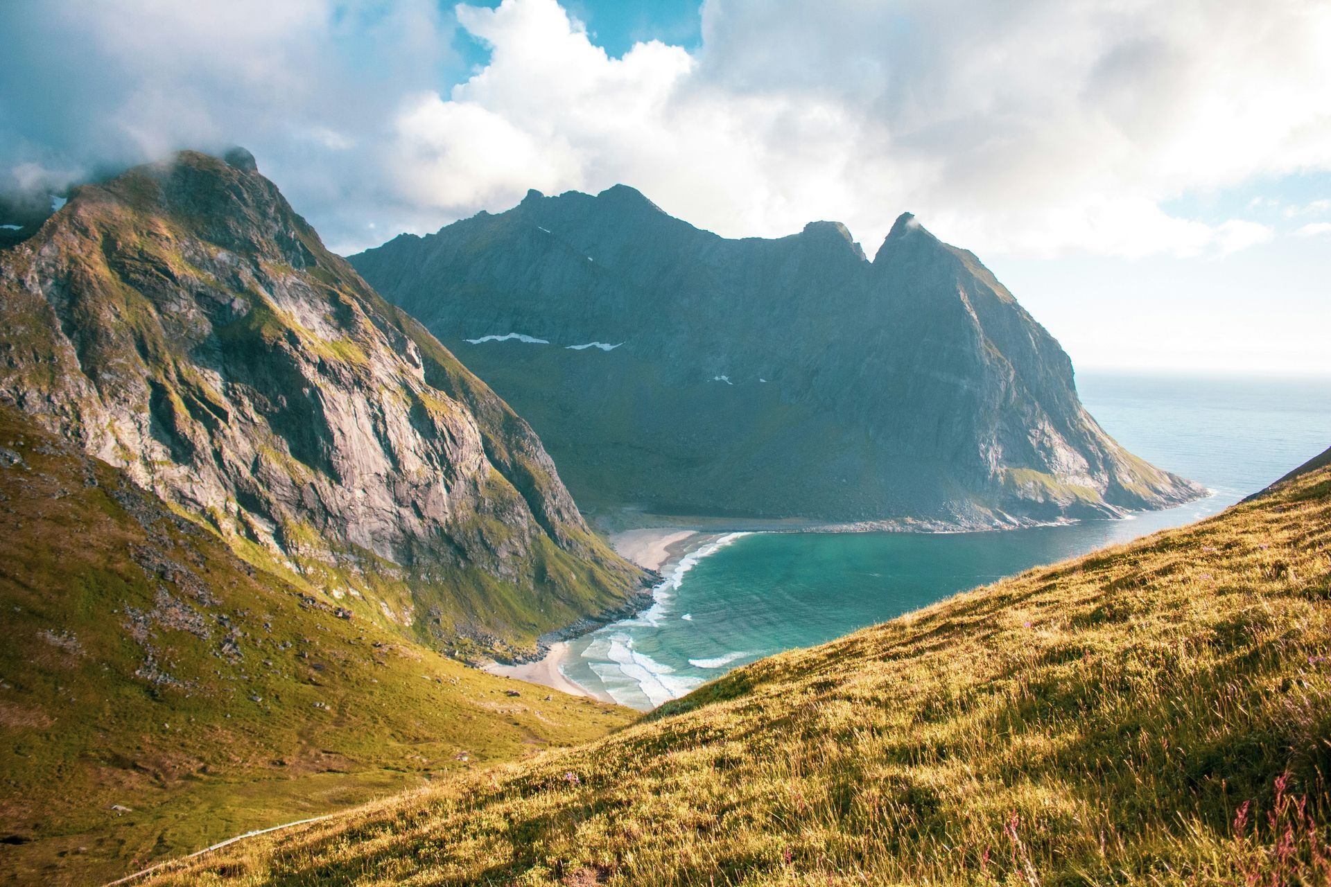 Mountains overlooking a turquoise beach. Green hills and grass in foreground in Lofoten, Norway.
