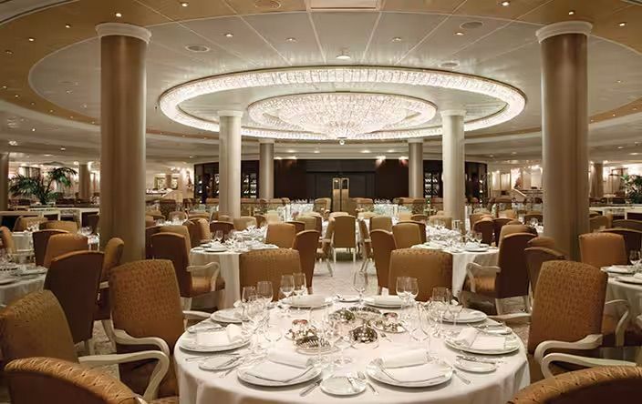 A large dining room filled with tables and chairs and a chandelier on the Oceania Riviera cruise ship.