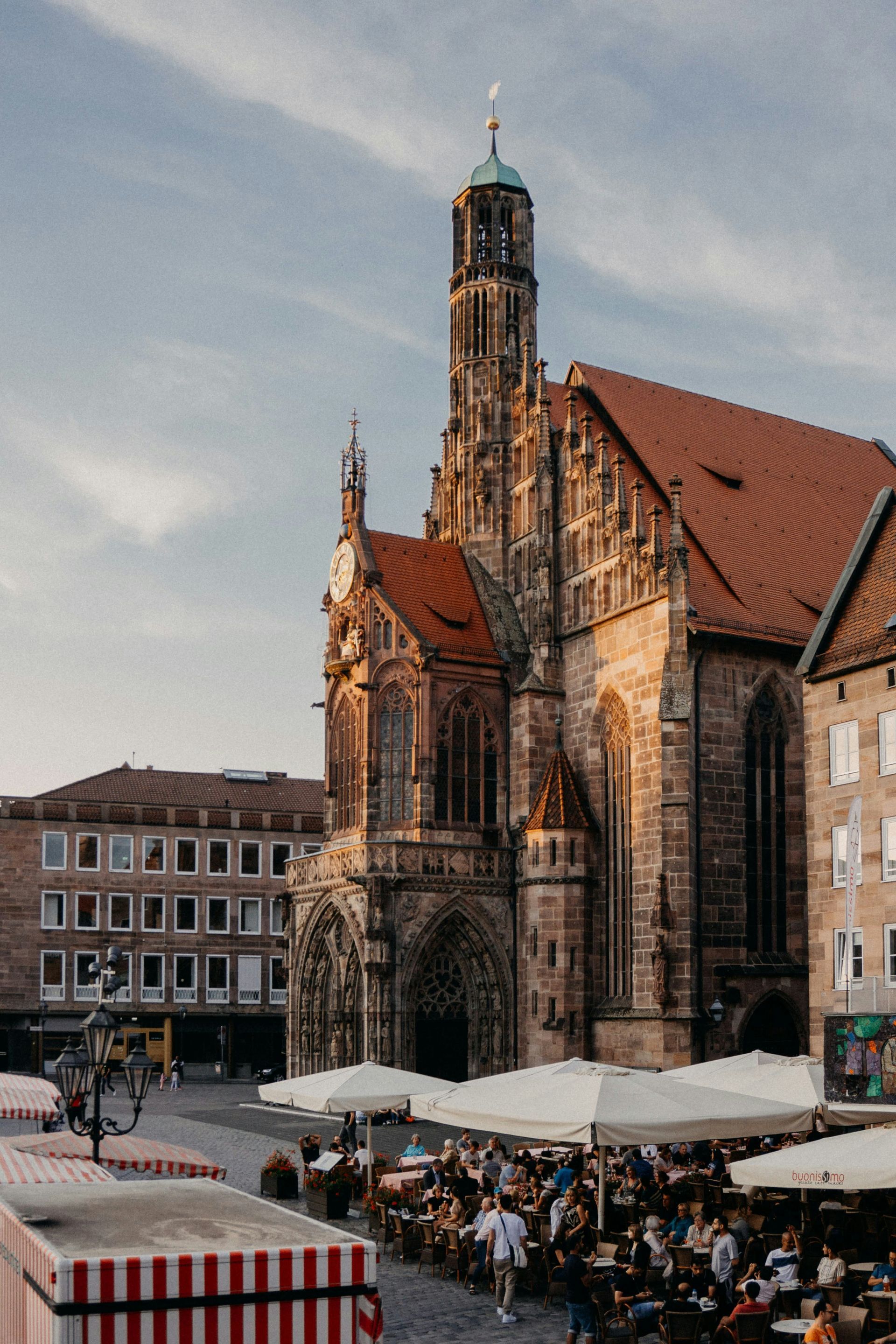 Church in Nuremberg, Germany, with red tile roof and tall ornate tower. Outdoor cafe in foreground.