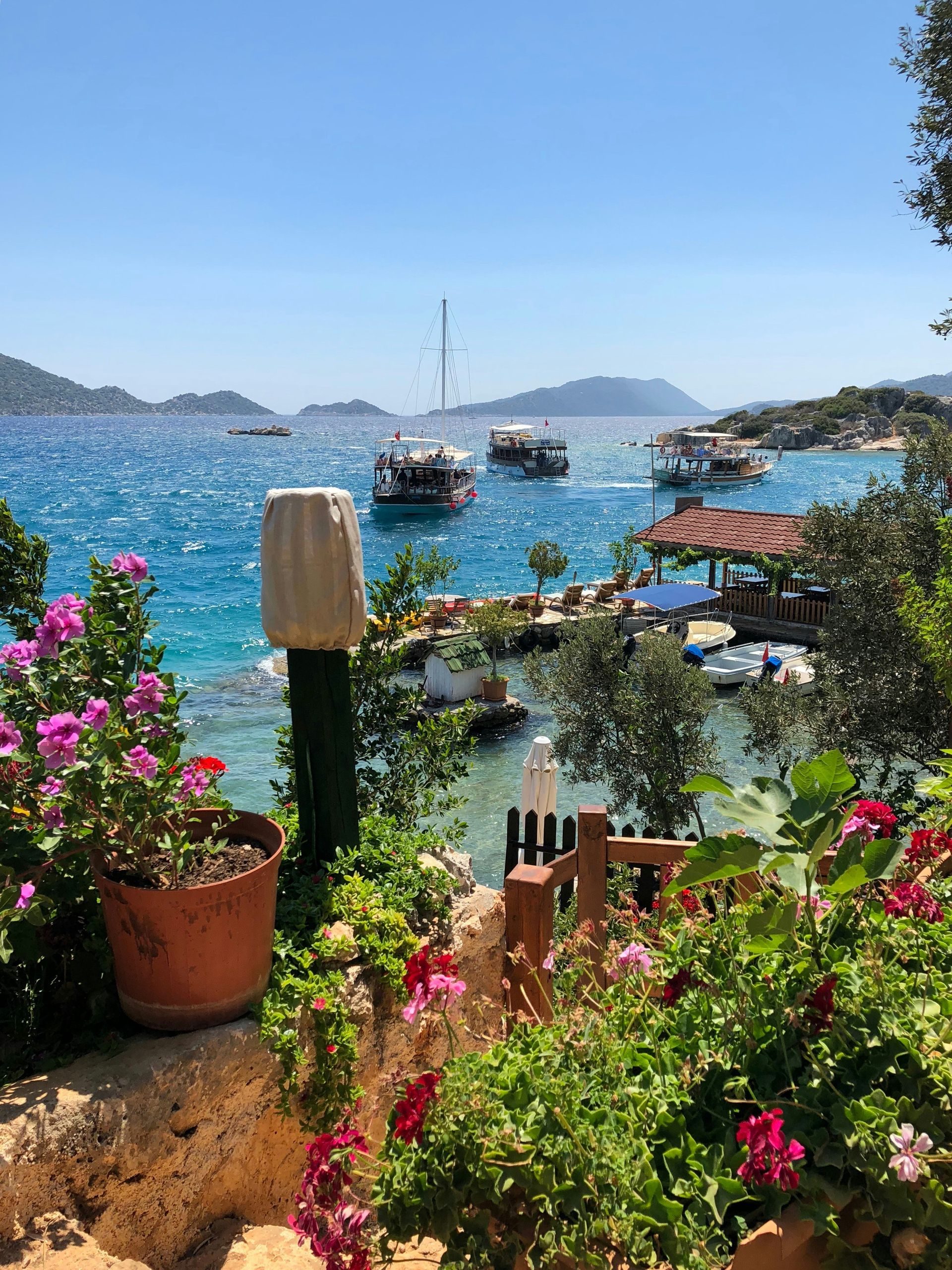Bright blue ocean vista with boats, lush greenery, and blooming flowers in Antalya, Turkey.
