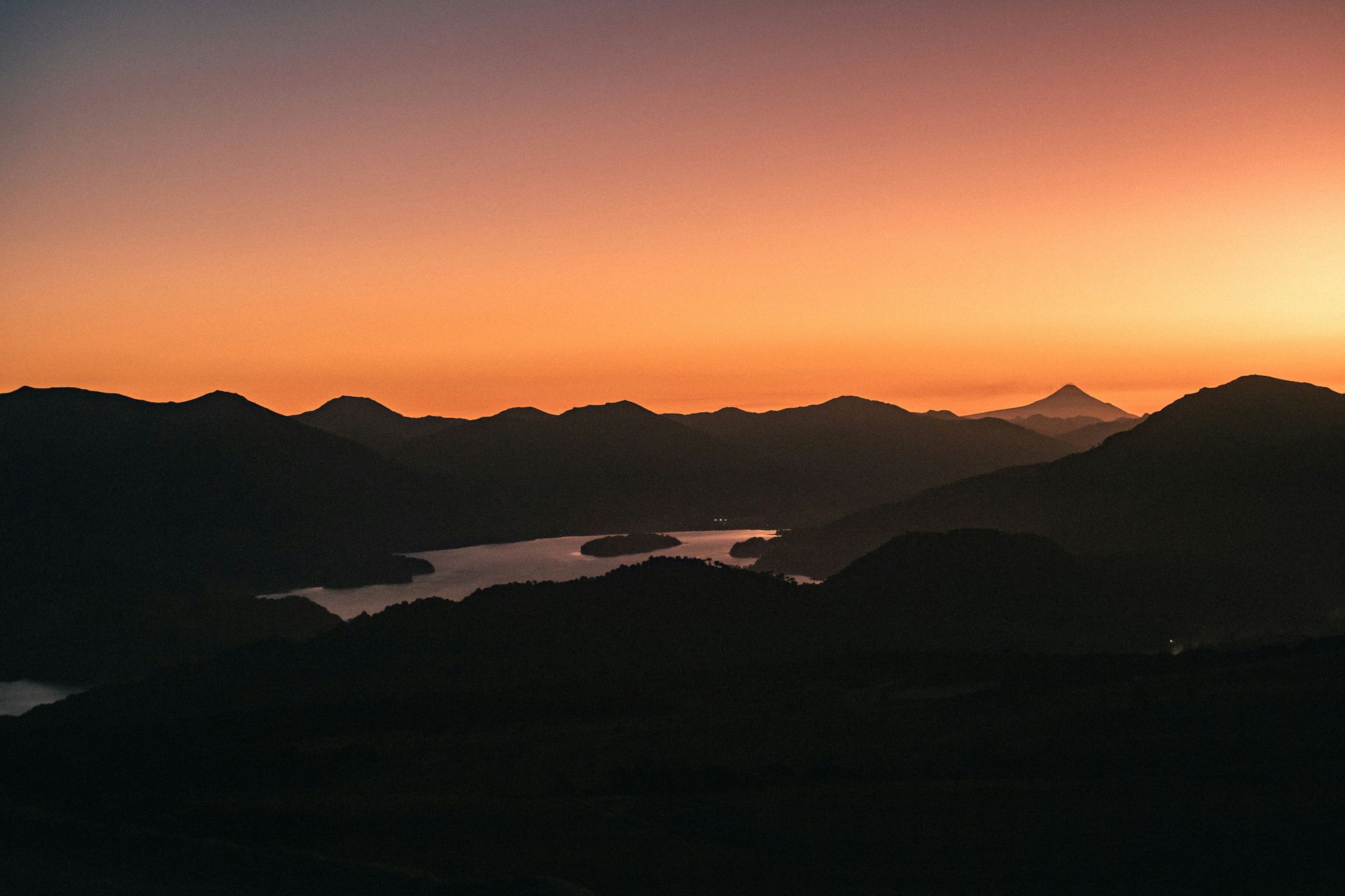 Sunset over dark mountain range and lake; orange and purple sky in Los Lagos, Chile.